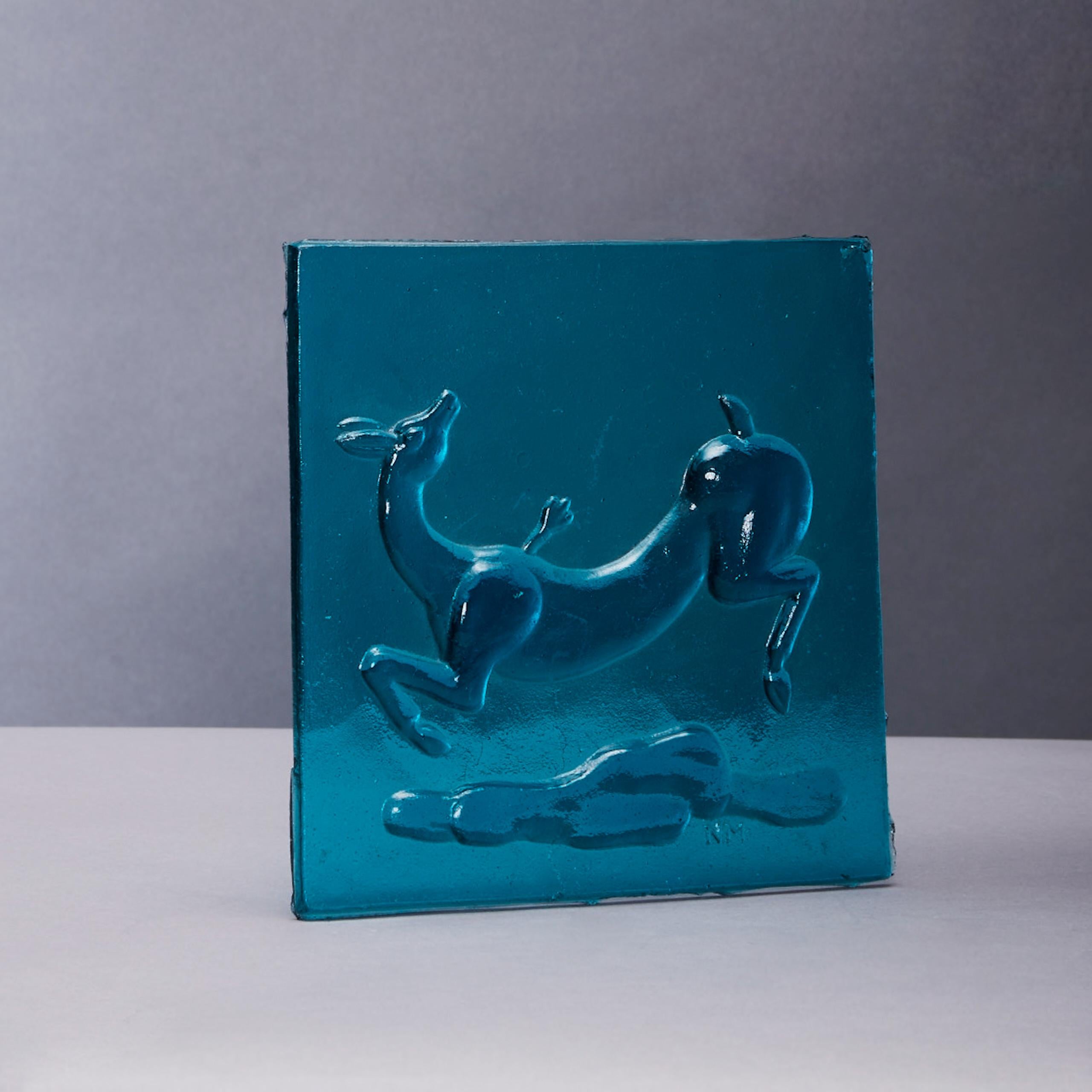 Piastrella in vetro stampato blu acqua di Napoleone Martinuzzi (1892-1977) del 1930 circa per Venini, marchio stampato 'NM',  raffigurante una gazzella ferita  .
Un esempio di questo modello è stato utilizzato in un progetto di lampada da terra per