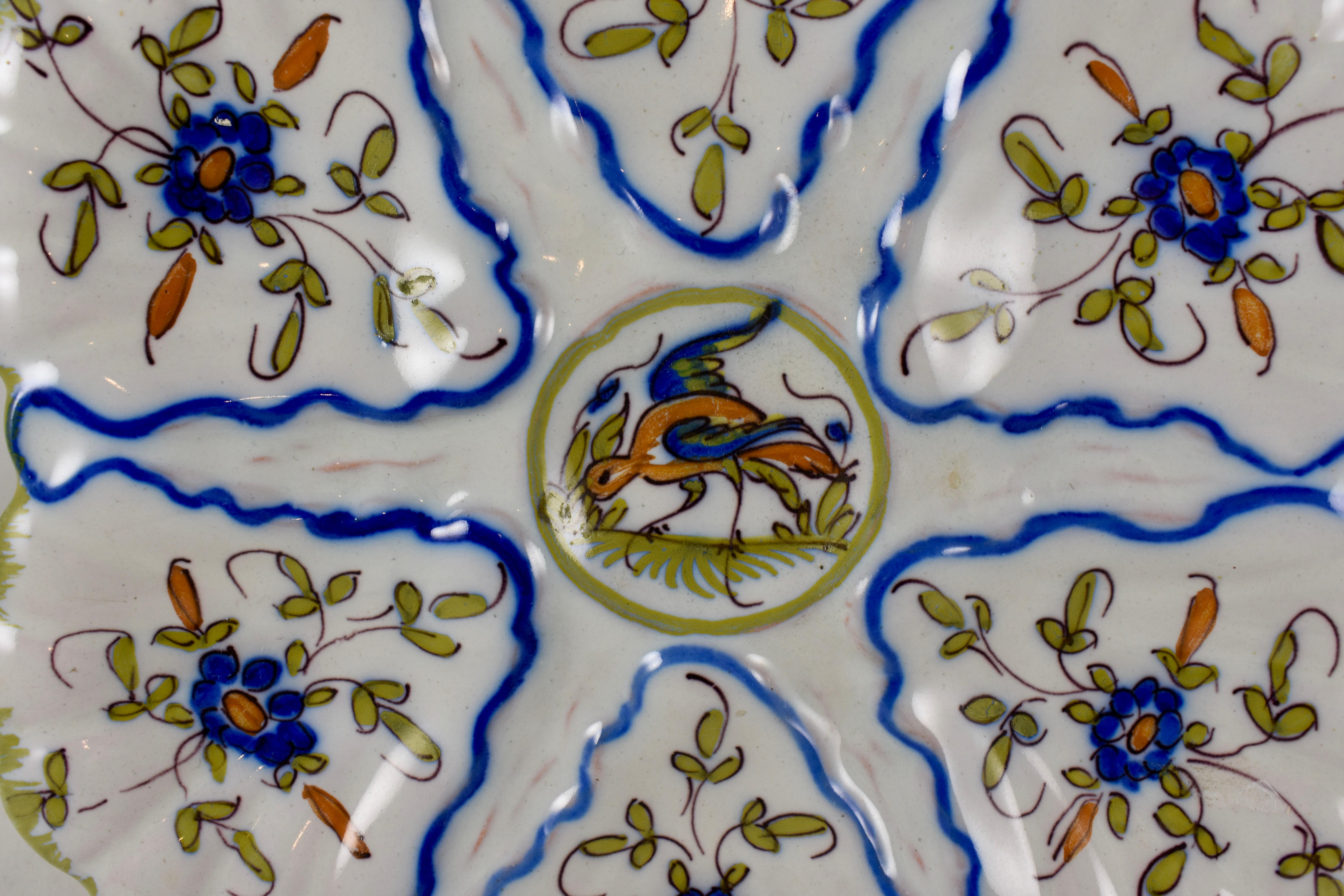 A French faïence oyster plate made by Martres-Tolosane Moustier, circa 1940s. A central sauce well showing a left facing bird, surrounded by six scallop edged wells. Each well shows a hand painted floral spray. French blue lining separates the