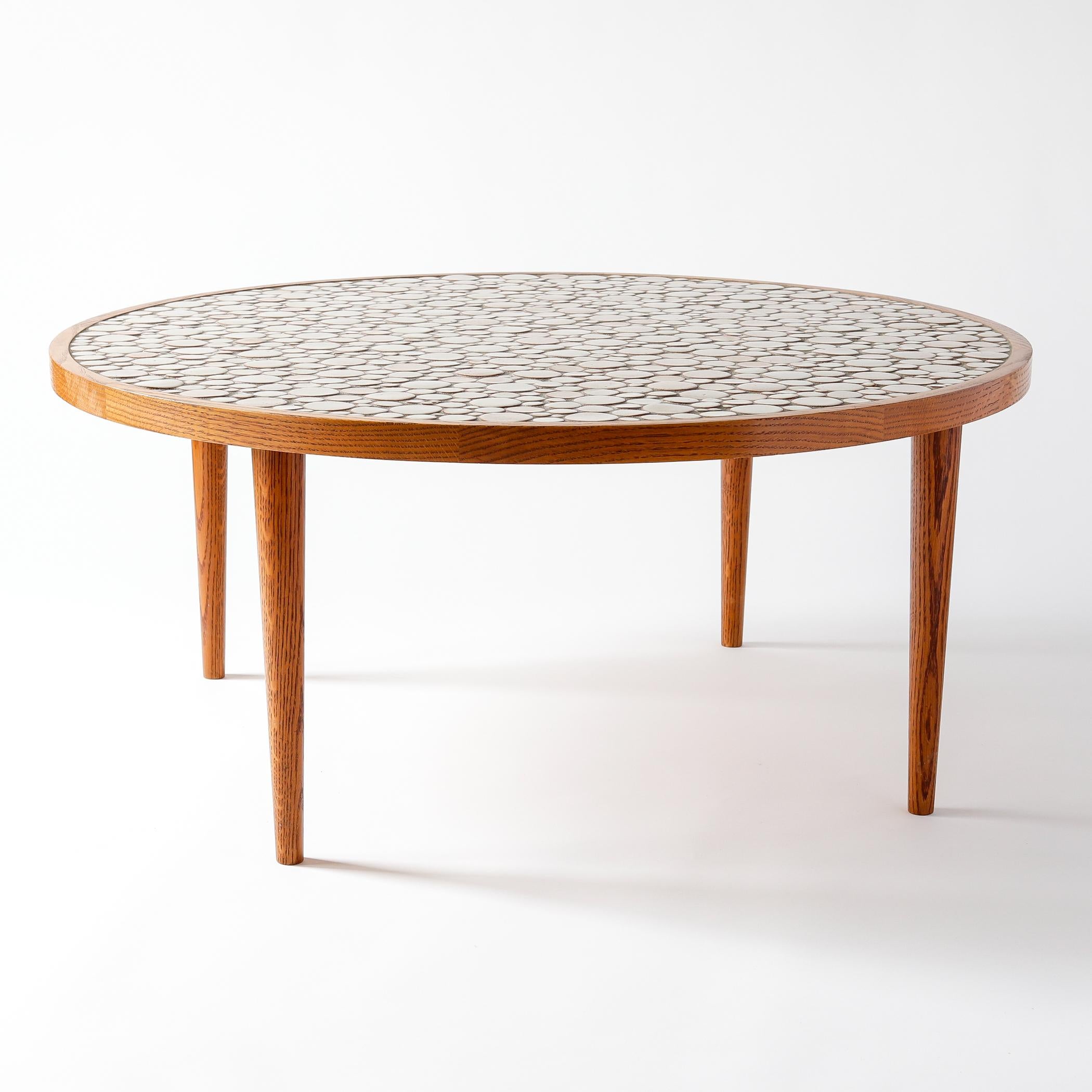 Mid-century oak and ceramic coffee table designed by Jane and Gordon Martz for Marshall Studios of Indiana. The oak frame has a circular top set with round tiles of various sizes in shades of beige.

Measures: 16 inches high, 36 1/2 inches