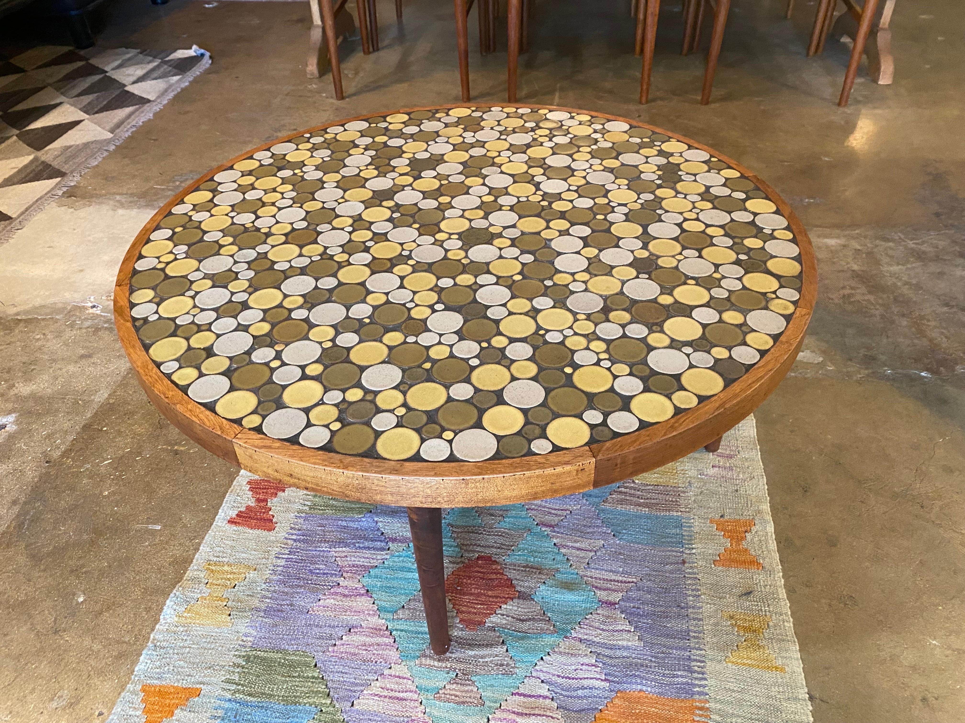 Mid-Century Modern ceramic coin tile top coffee table, designed by Jane and Gordon Martz for Marshall Studio. features a walnut frame with an inlaid ceramic round top. Coin tiles in earthy shades of olive, light yellow, and grey. This table is in