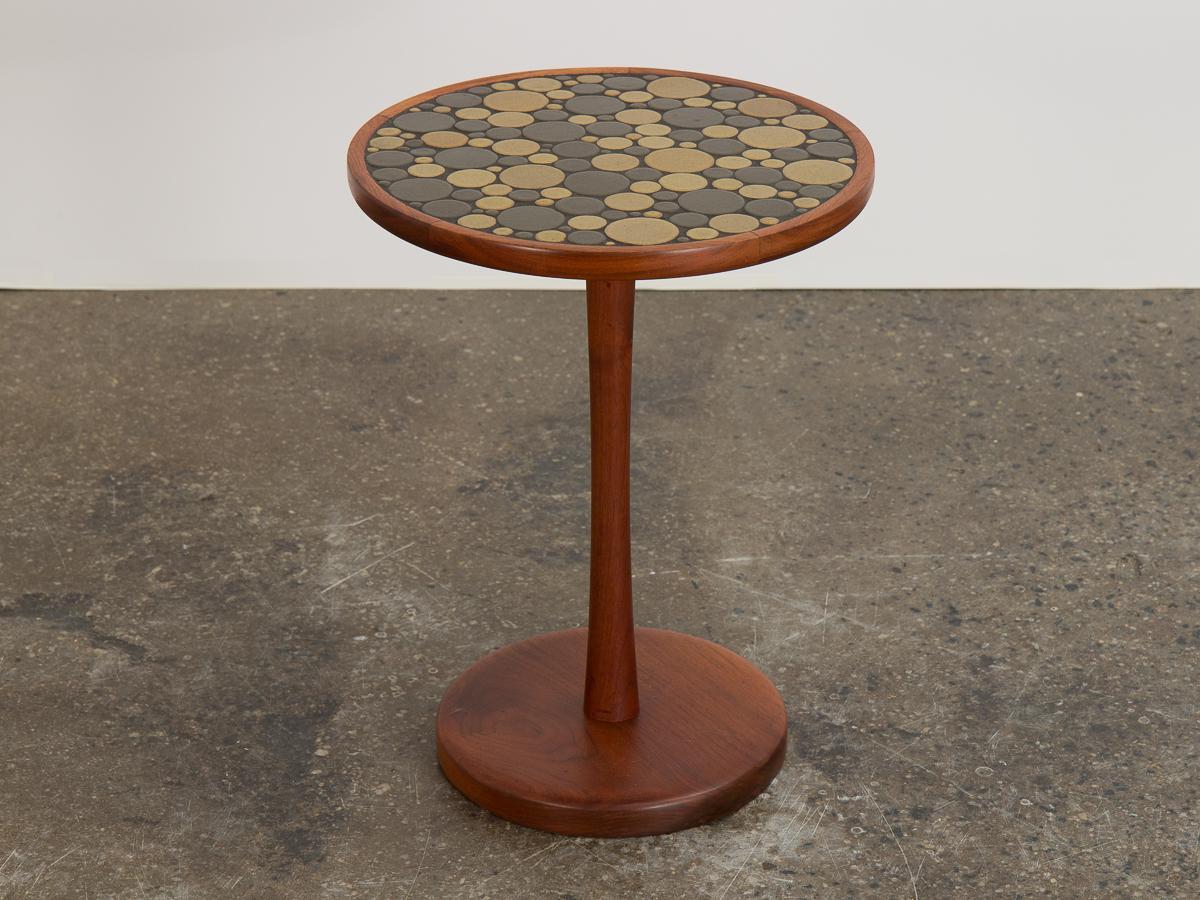 Ceramic coin tile top side table, designed by Jane and Gordon Martz for Marshall Studio. Beautiful turned walnut pedestal frame with signature inlaid ceramic round top. Known for their textured ceramic mosaics on minimal wood forms, this occasional