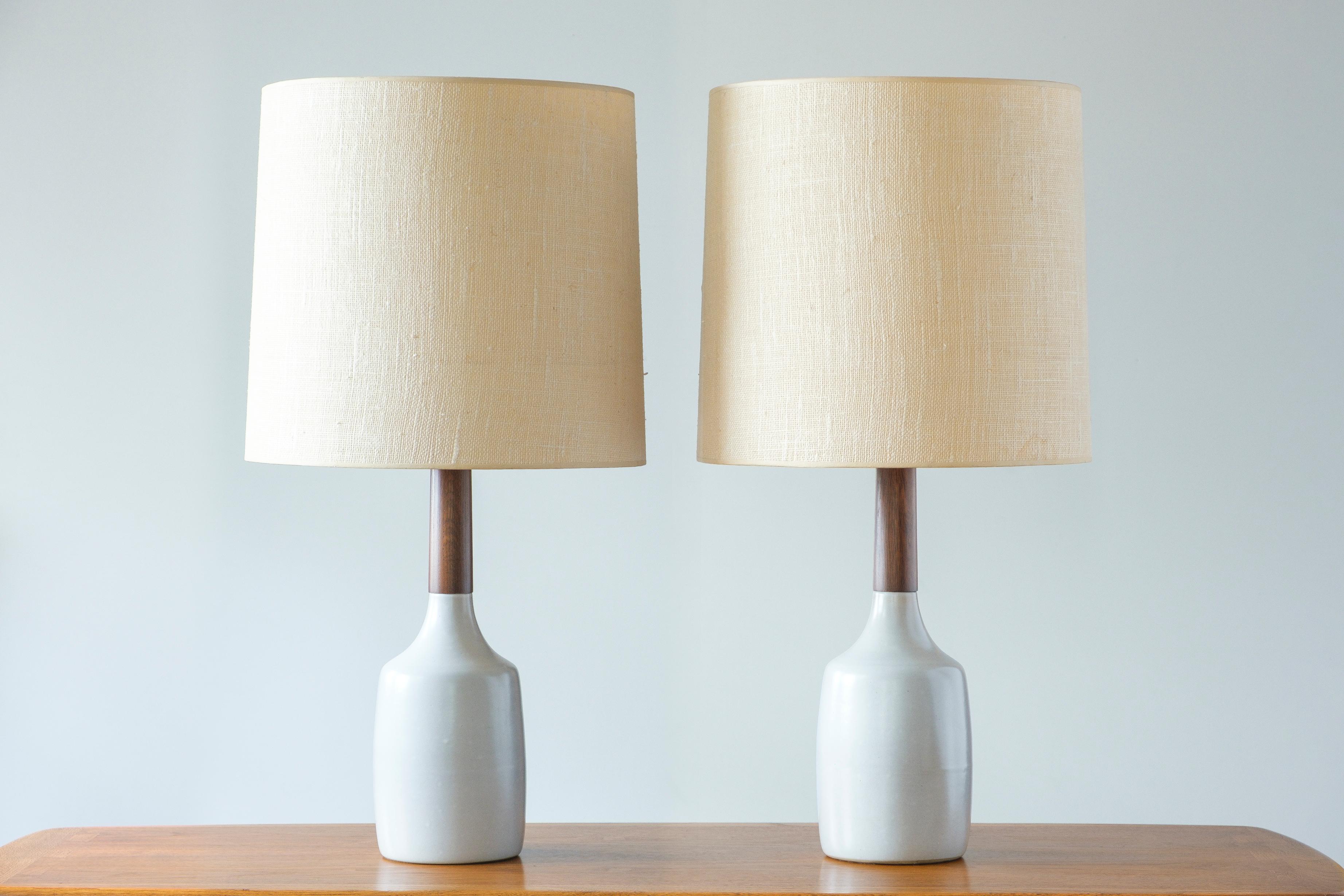 What is it?
—
A pair of ceramic and teak table lamps (shades not included) from the masters of mid century lightning – Gordon and Jane Martz.

These signed Martz lamps come in a satin white glaze with small flecks of red and blue. The ceramic base