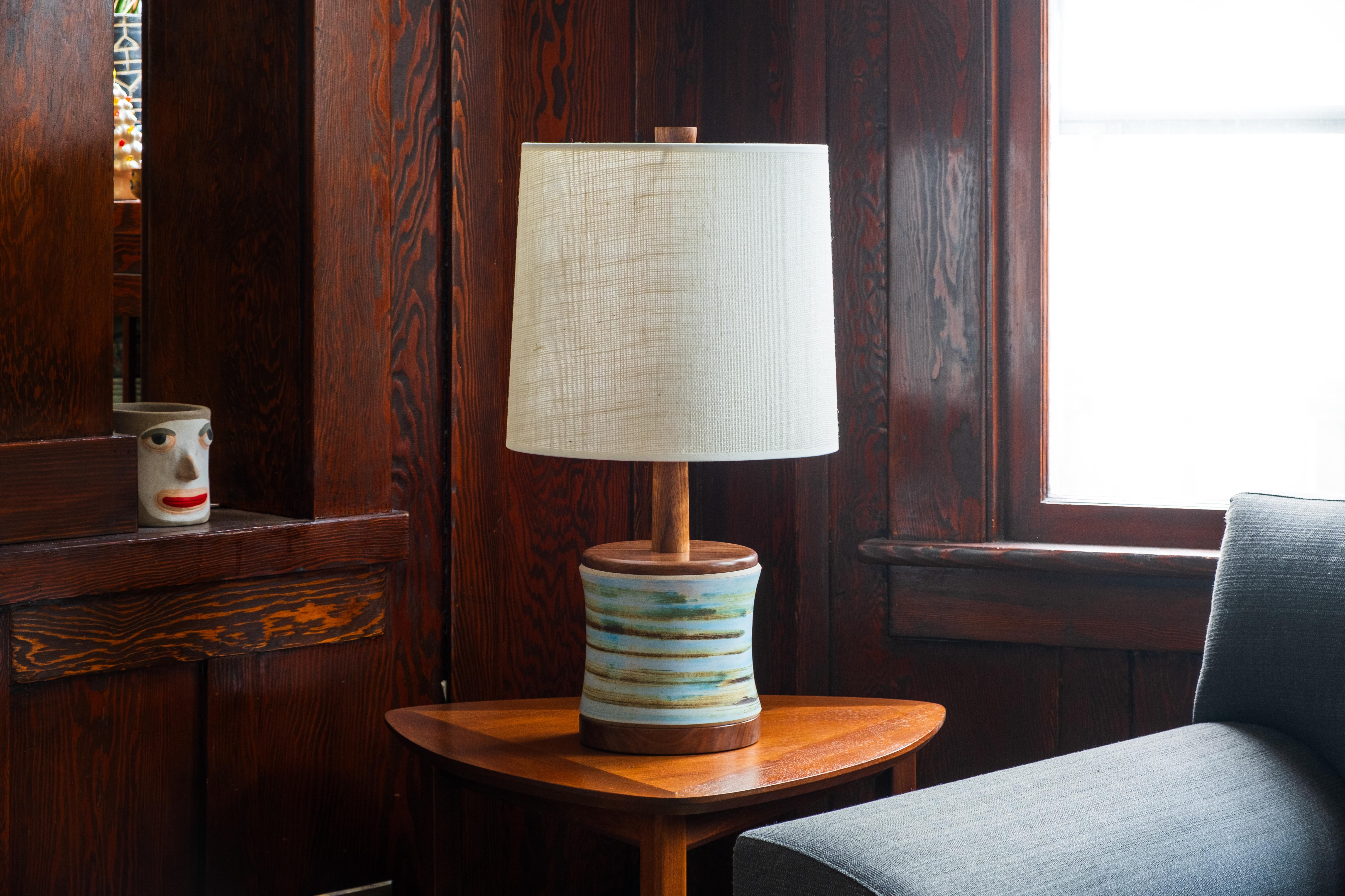 Qu'est-ce que c'est ?
-
Cette lampe de Gordon et Jane Whiting se caractérise par une base émaillée d'un blanc doux, accentuée par des rayures horizontales dans des bleus et des bruns sourds. Les rayures encerclent la base en céramique et se fondent