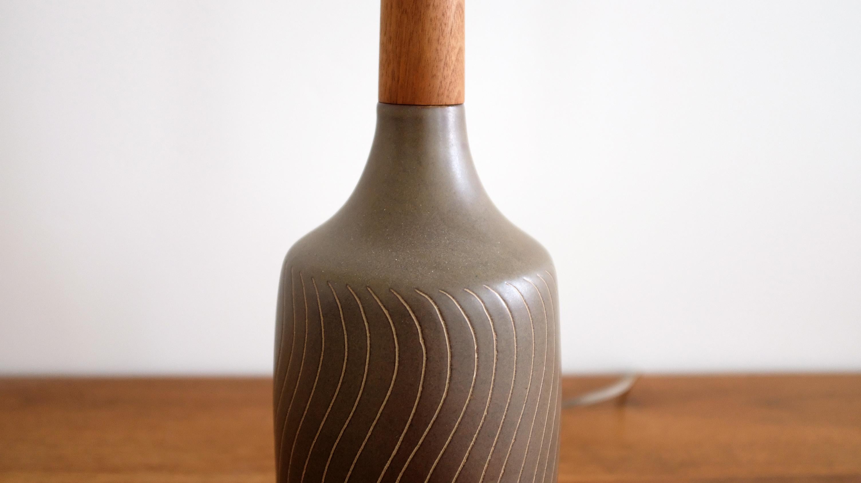 Uncommon matte green glazed ceramic table lamp by A unique table lamp ceramicist duo Jane and Gordon Martz, for Marshall Studios, 1960s. 

Features a matte green, glazed body with incised organic patterns, and a patinated walnut neck and finial. The