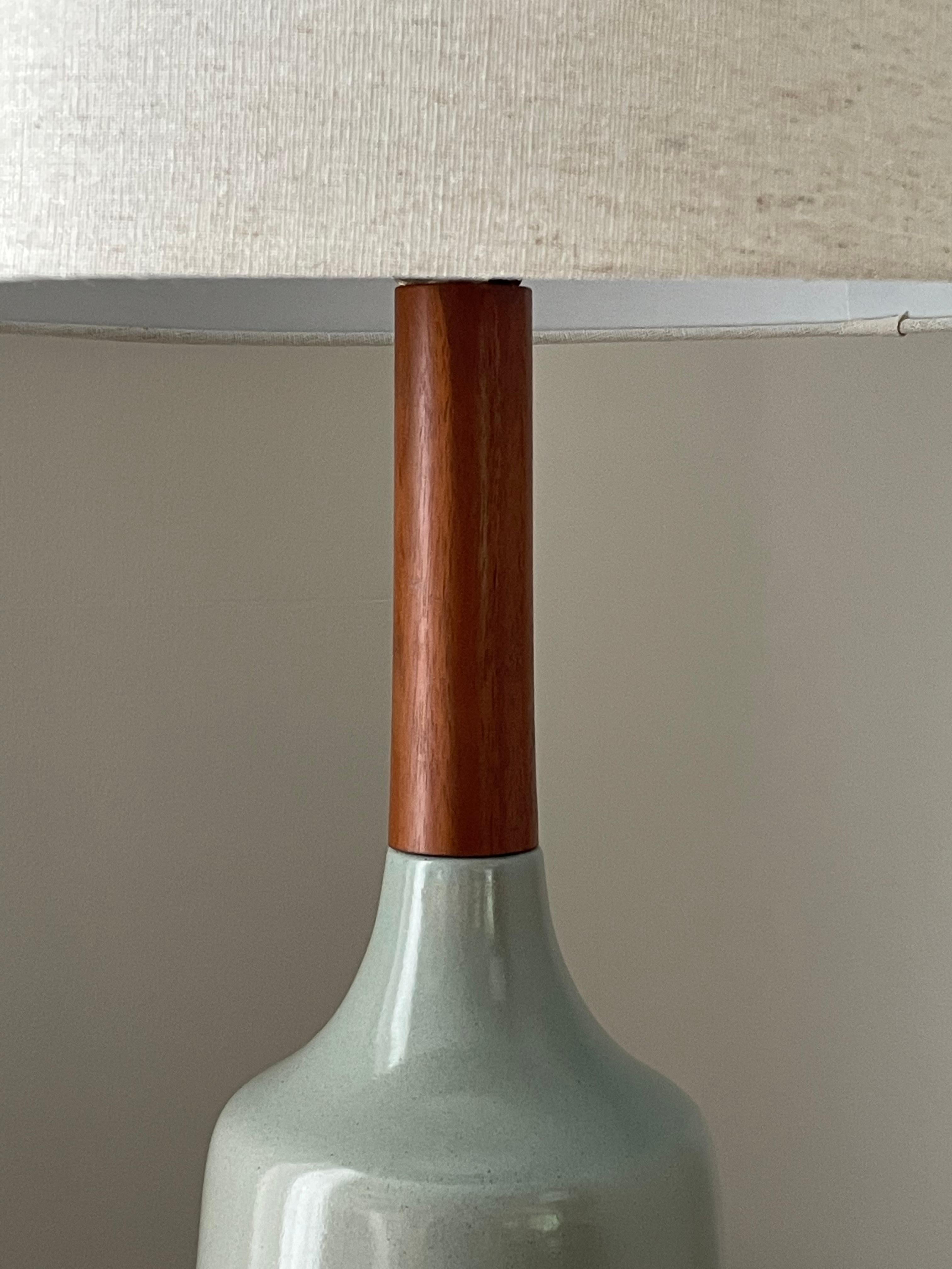 A unique table lamp designed by famed ceramacist duo Jane and Gordon Martz for Marshall Studios. Features a glazed body with a blue/ tan hue towards the bottom that turns into baby blue towards the neck. Long walnut neck and matching finial.