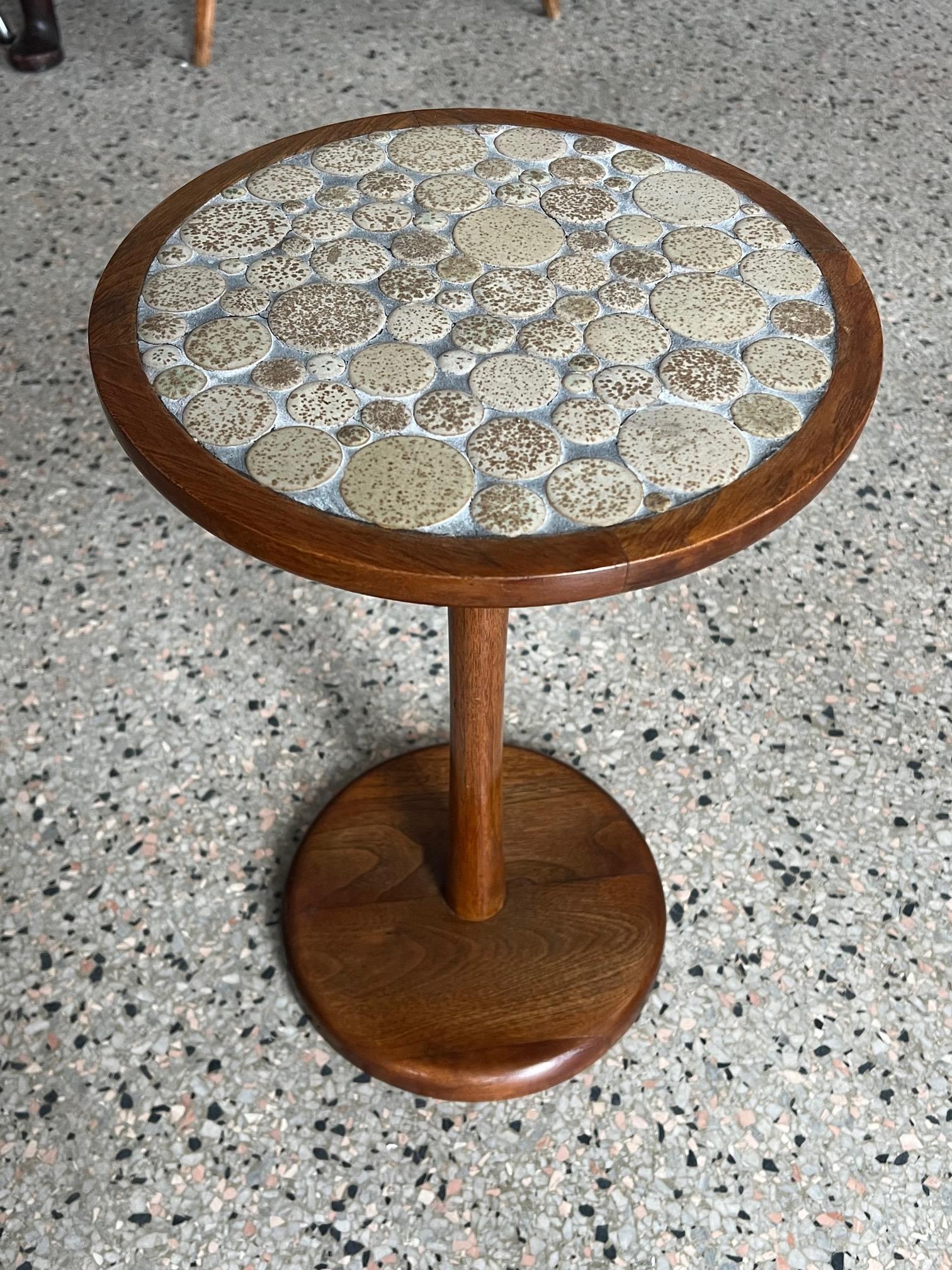Ceramic coin shaped tile top side table, designed by Jane and Gordon Martz for Marshall Studio. Beautiful turned walnut pedestal frame with inlaid ceramic round top. The Martz's are known for their ceramic mosaics and this occasional table is a very
