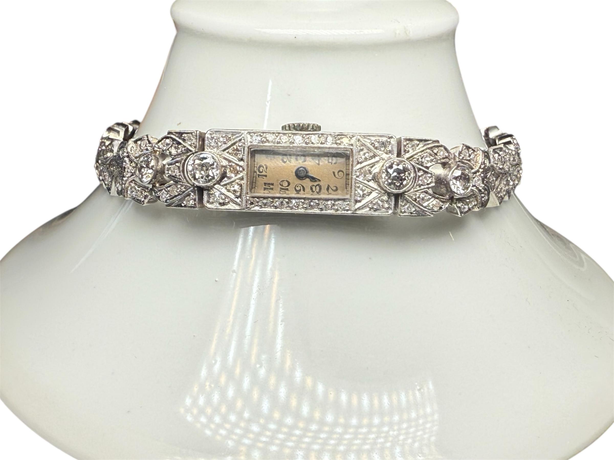 Se trata de un Reloj de pulsera de mujer Marvel de platino y diamantes. Presenta una caja rectangular de platino con esfera de color beige que tiene números arábigos y   Manecillas de hora/minutos en color. Un cristal de material acrílico cubre la