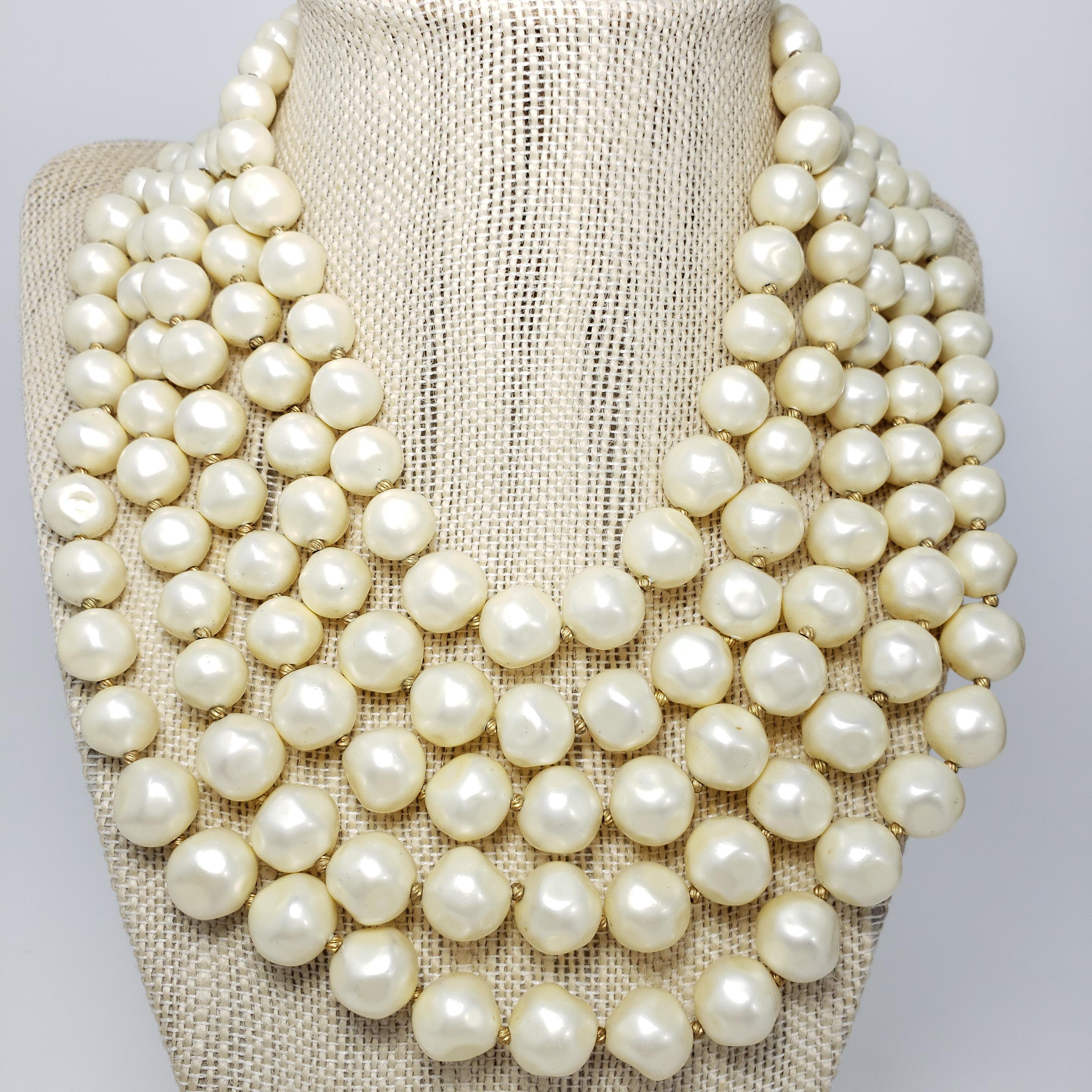 A luxurious multi-strand necklace by Marvella. Features five strands of graduated faux pearls. The colorful clasp features a centerpiece faux mother of pearl, decorated with faux seeded pearls and polished mottled salmon, turquoise, and deep blue