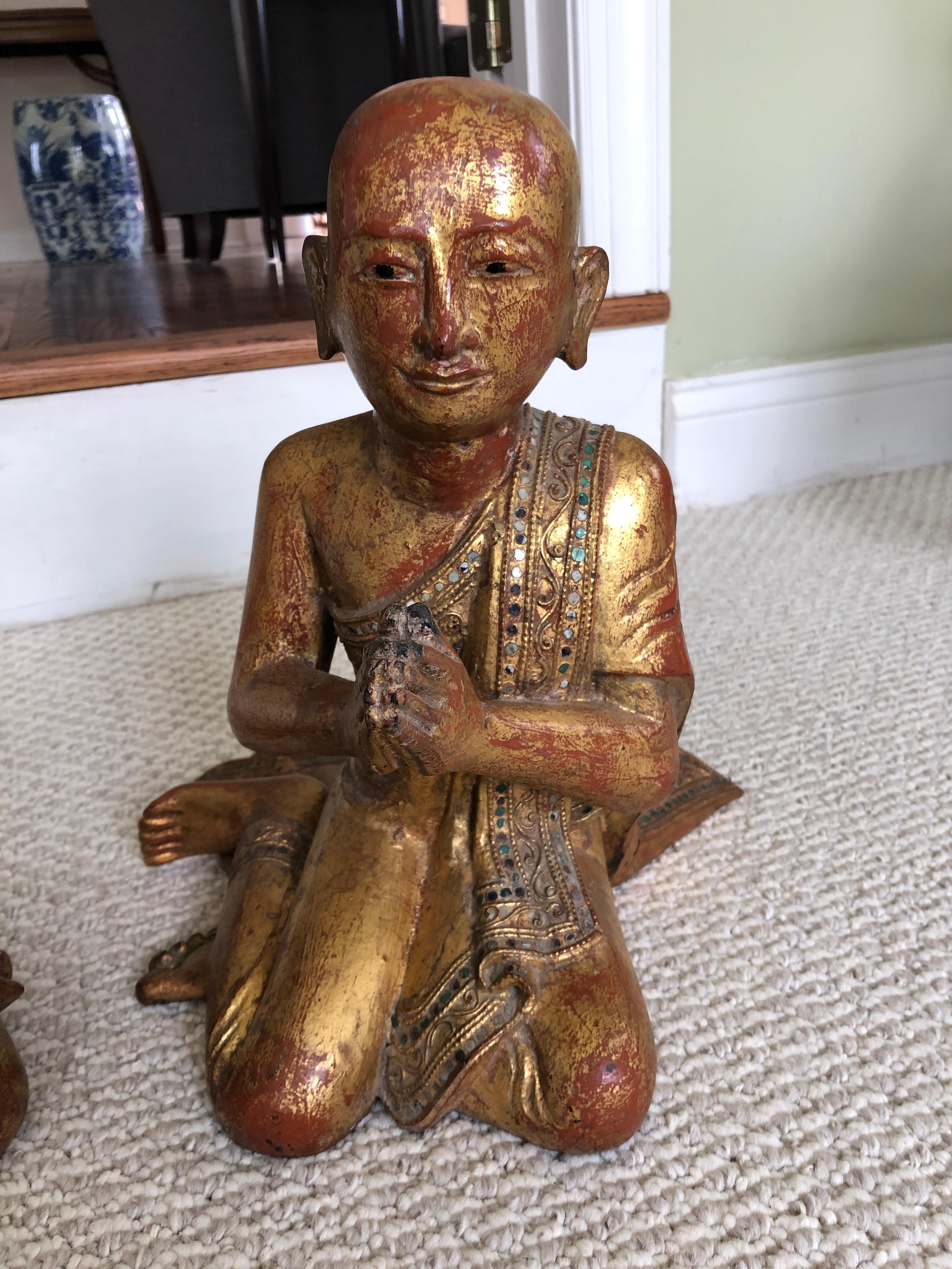 A pair of gorgeous seated monk sculptures, one listening and one praying, having gilded carved wood with wonderful red under paint and lovely colored glass inlaid embellishments. Mandalay period originally from Burma. Each monk is unique with