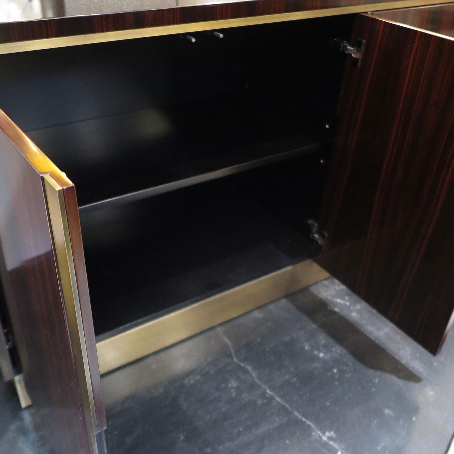 Sideboard in high-gloss dark Macassar ebony with metal base and door details. Five doors have touch-latch hardware and vertical angular brushed brass divisions. The cabinet doors open to a single space with an adjustable shelf that runs the length