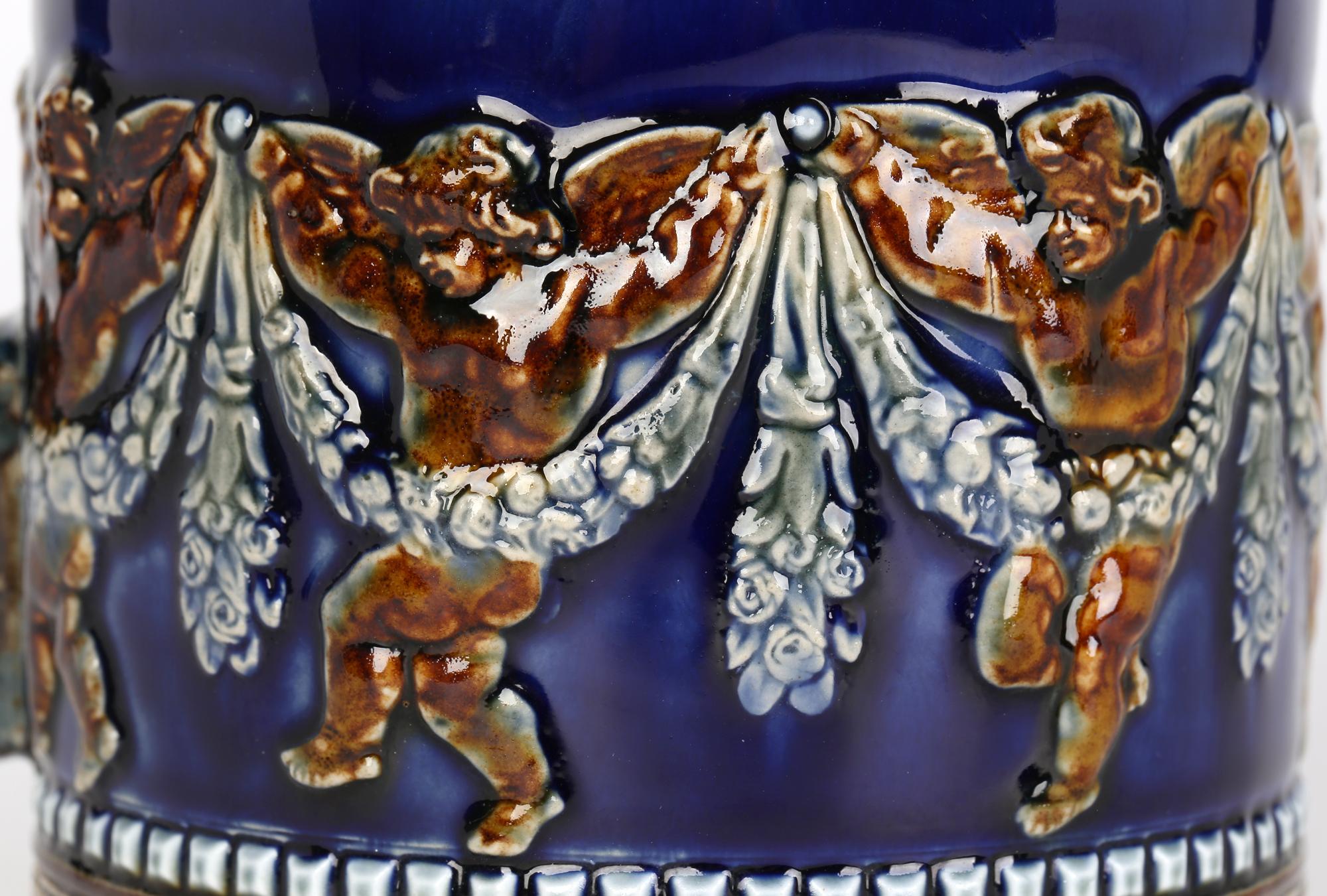 Inusual jarra grande Doulton Lambeth del Aesthetic Movement, decorada con querubines danzantes, obra de Mary Aitken y asistida por Harriette Knight, fechada en 1883. La jarra de gres es de forma cilíndrica ancha, con un hombro en ángulo y una