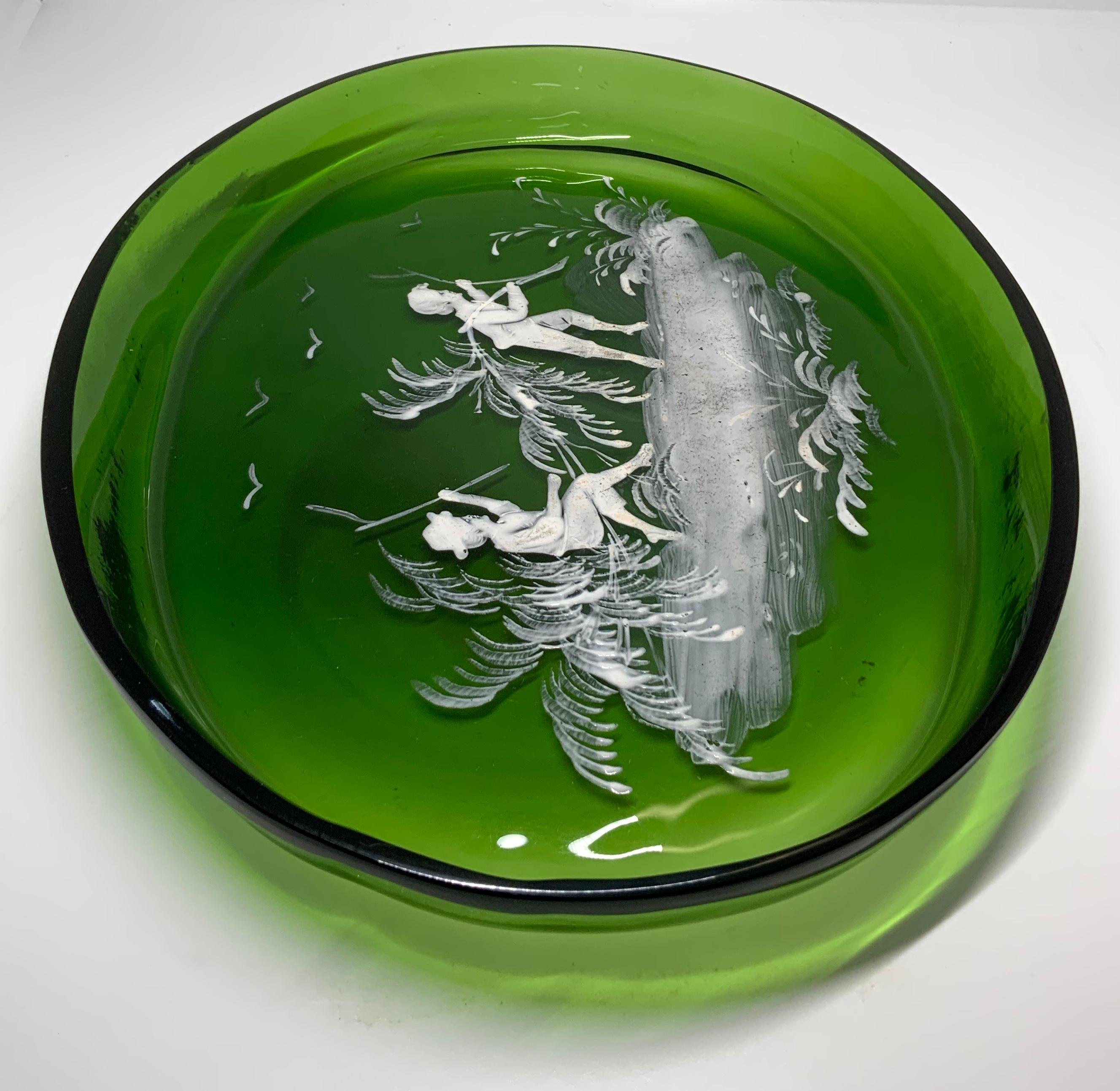 This is a Mary Gregory emerald green glass large oval plate. It is hand painted with white enamel featuring a scene of two boys- one boy is “riding” over a few bamboo branches while the other one is pulling them. There are some birds flying in the
