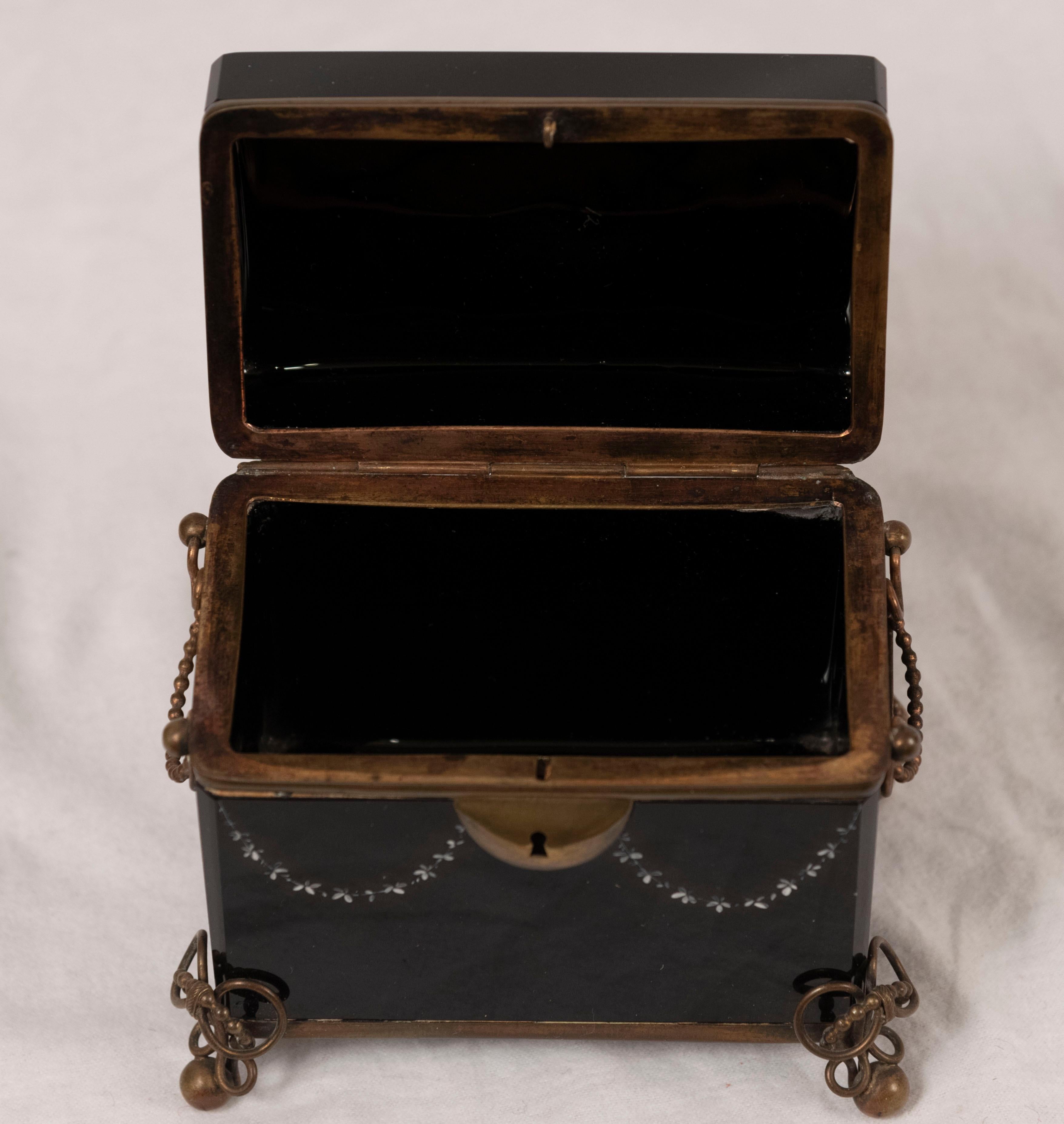 Mary Gregory enamel decorated black glass box in casket form. The lid is painted with a child jumping rope and set in a gilt metal stand.