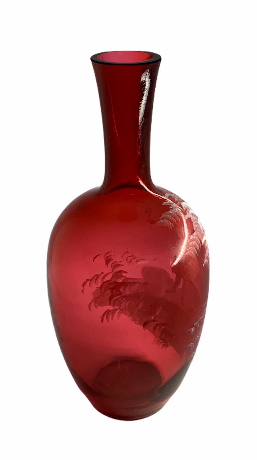Dies ist ein rotes Glas von Mary Gregory, das eine weiße Emailmalerei eines Mädchens zeigt, das im Wald Stöcke und Äste sammelt.