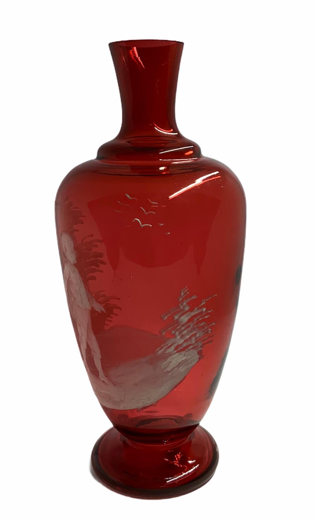 Questo è il vaso in vetro rosso di Mary Gregory con base rotonda e piedistallo. È raffigurato un dipinto in smalto bianco di un ragazzo che tiene un ramo con un fiore nella mano destra.