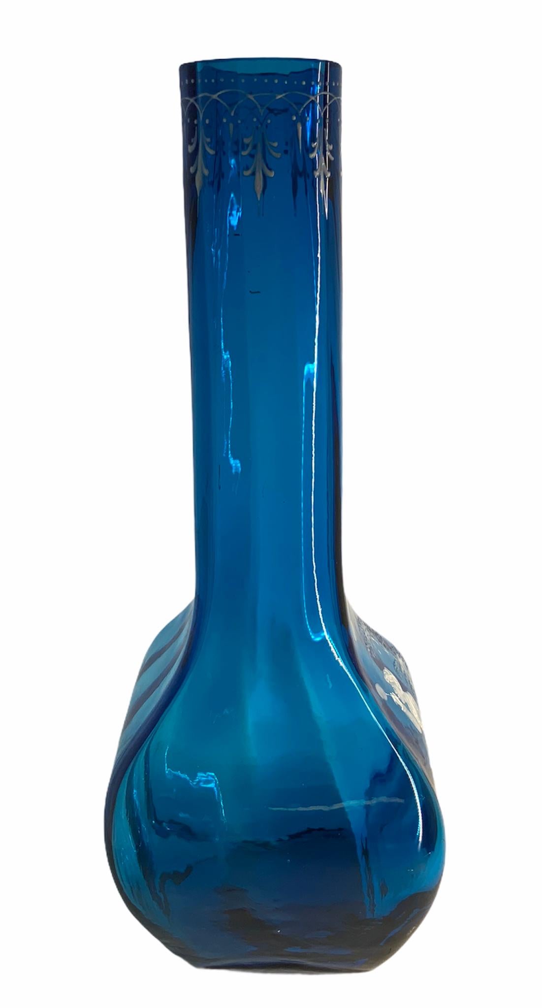 Vase à long col Mary Gregory en verre bleu royal. Il s'agit d'une peinture en émail blanc représentant un jeune garçon faisant des bulles dans la forêt. Il est également orné, sous le rebord supérieur, d'une guirlande de palmettes et de minuscules