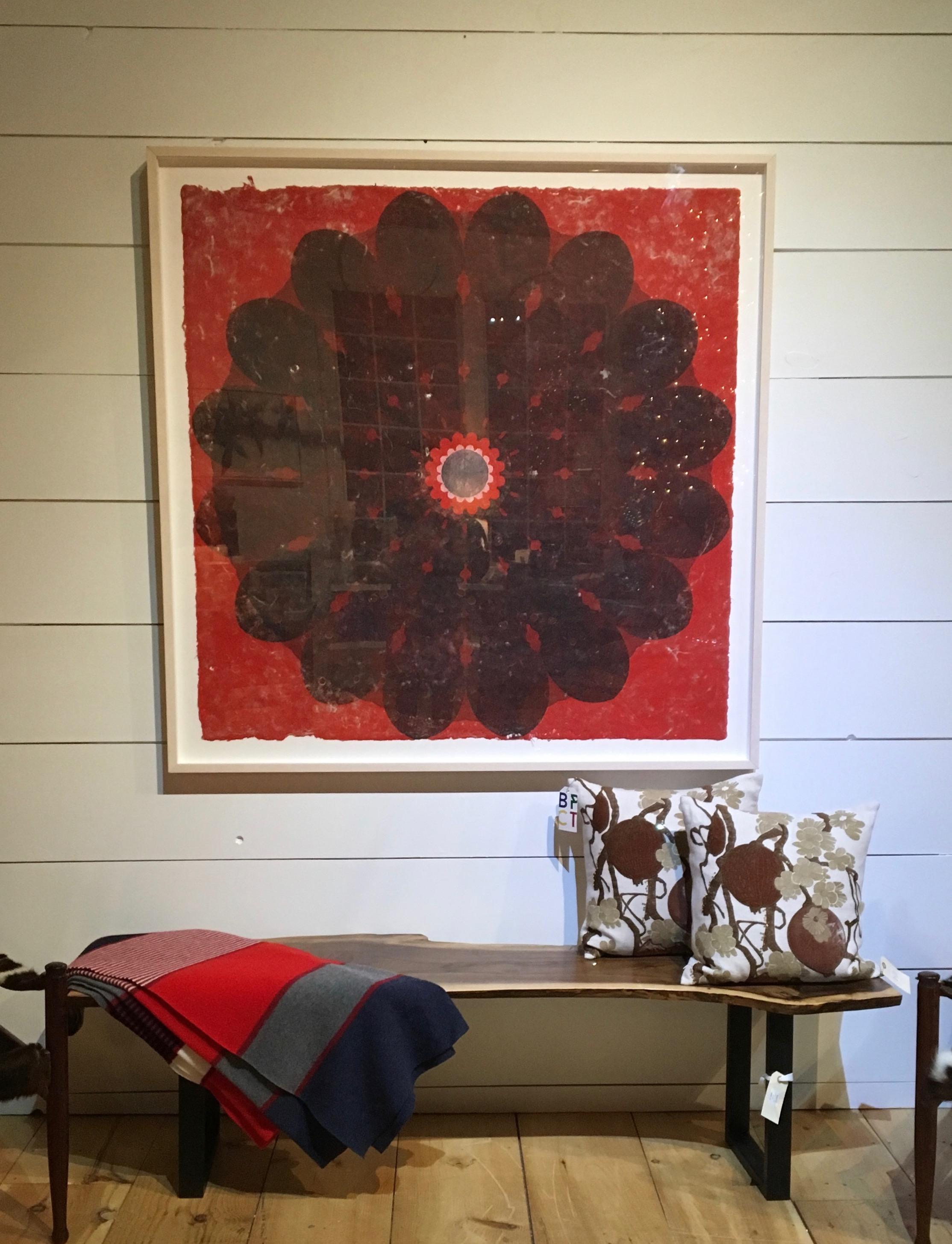 In this contemporary relief print on archival handmade paper, a circular, botanical mandala shape with petal-like edges in dark grey is dramatic and eye-catching against the brilliant red background. A circle surrounded by smaller petal shapes is at
