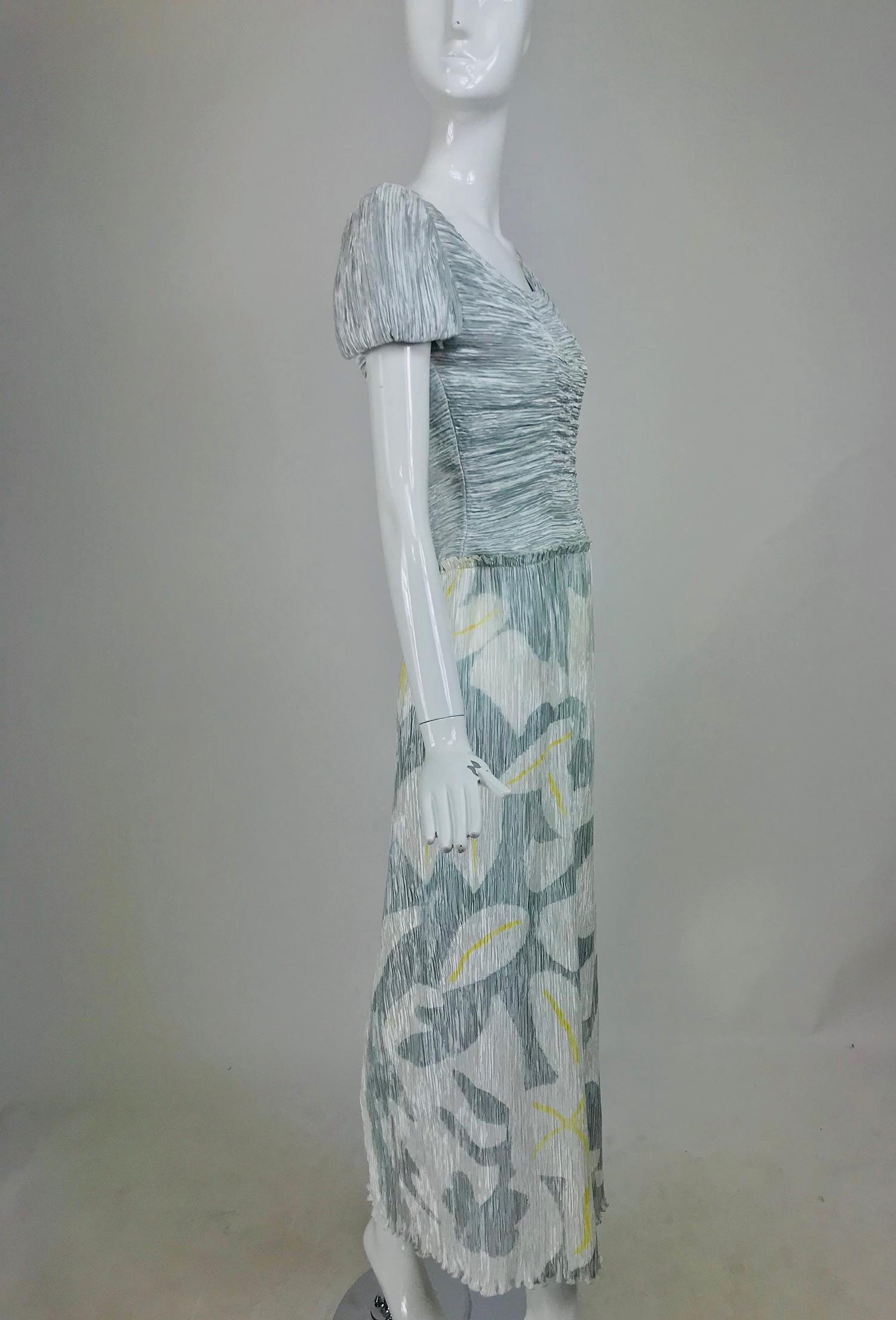 Mary McFadden Couture, pleated and painted evening gown in light and dark silver blue grey, the long pleated skirt has a modernist flower and vine dow the right side, the flowers have yellow centers. The bodice is horizontally pleated with short