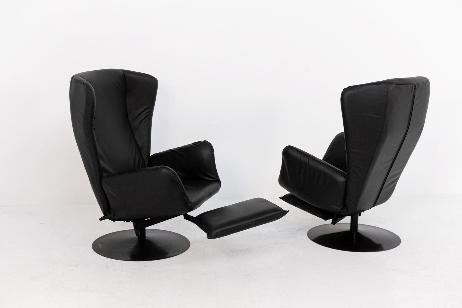 Paire de fauteuils excentriques en cuir noir des années 1970. 
La paire de fauteuils a été récemment restaurée. Les fauteuils ont plusieurs particularités, notamment les oreilles au-dessus du dossier. Autre particularité, le repose-pieds à coussin