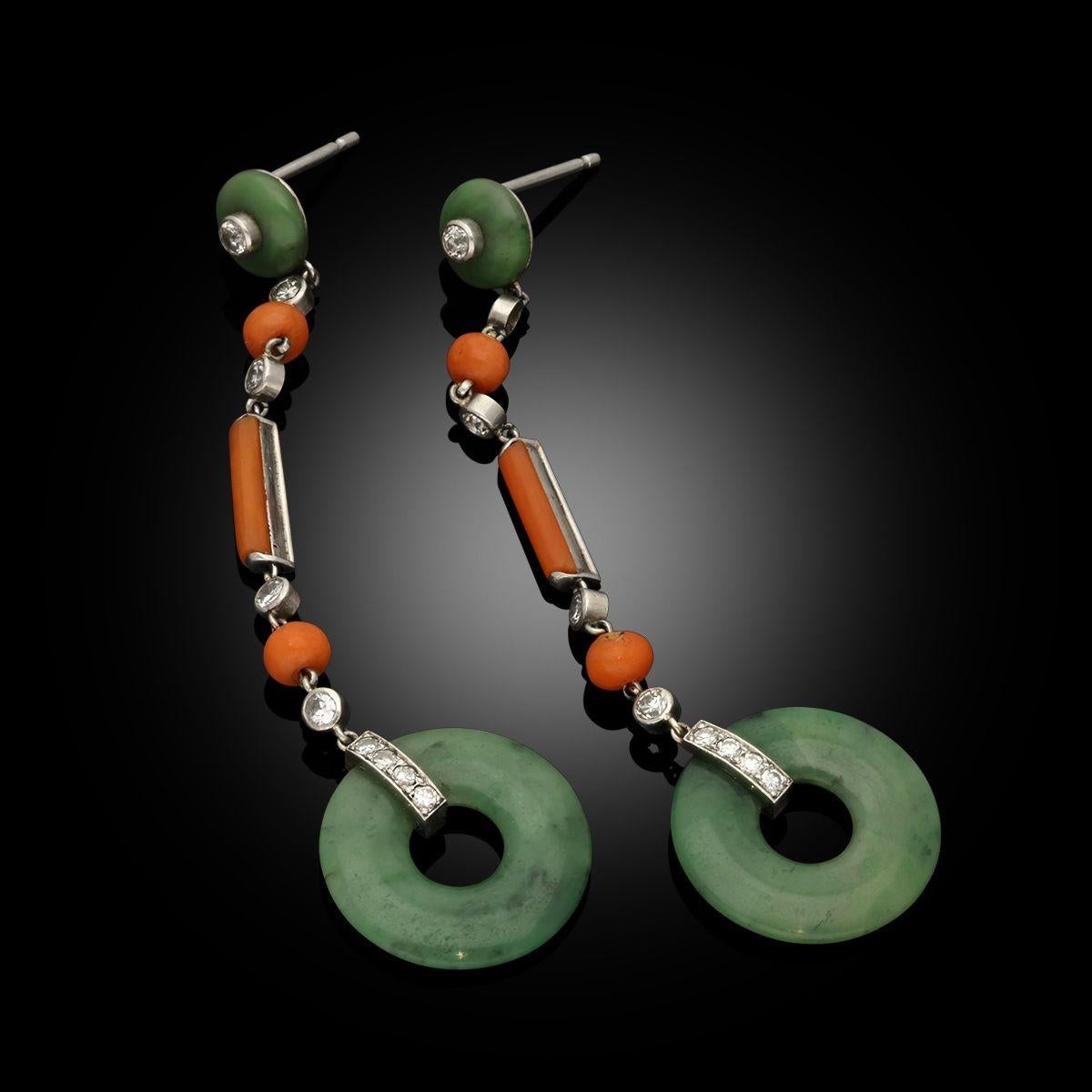A pair of Art Deco jade, coral and diamond long drop platinum earrings by Marzo, circa 1925. The earrings are long drop earrings with alternating discs of natural green jadeite, coral beads and round old cut diamonds, with circular polished discs of