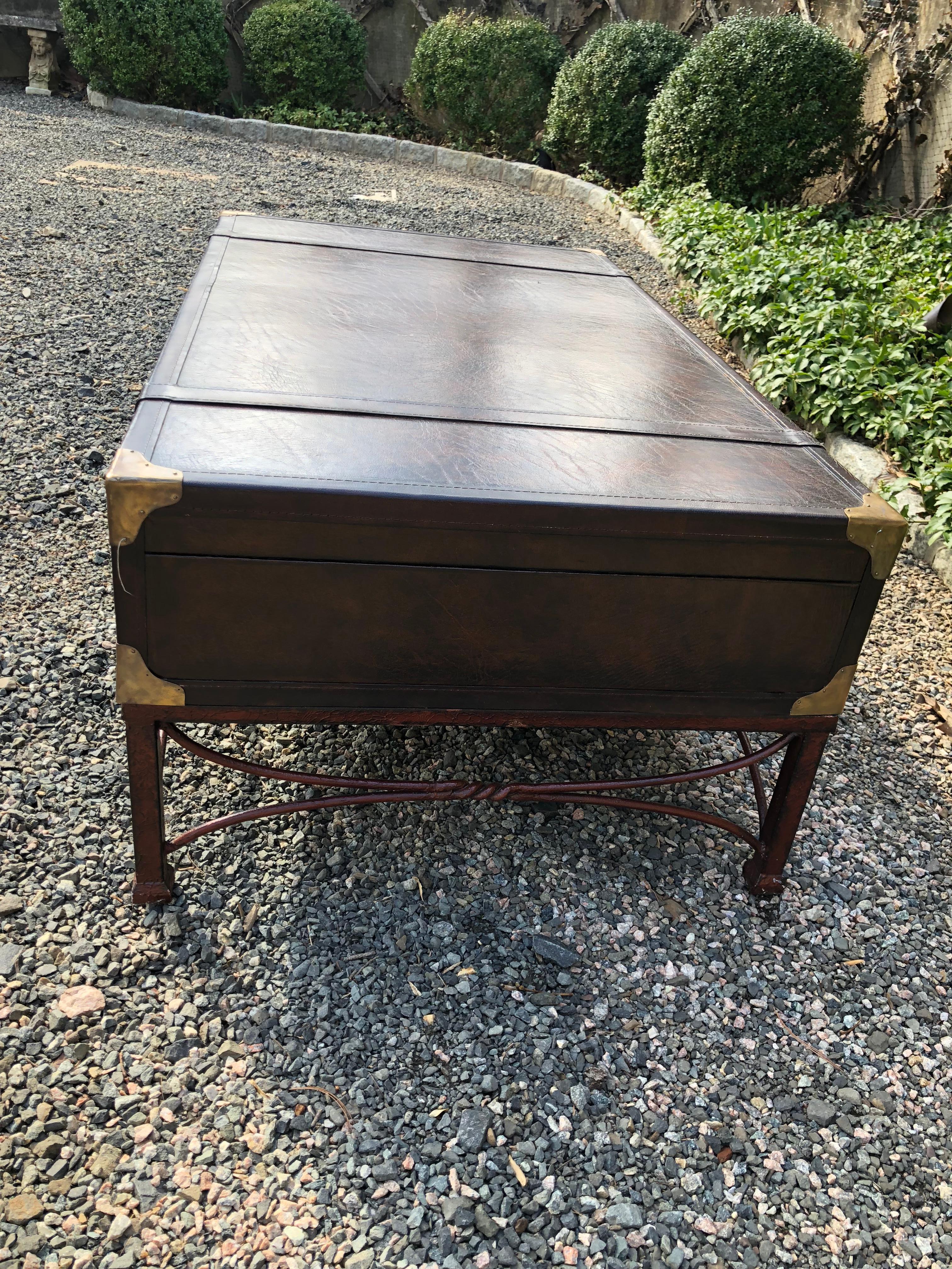Ralph Lauren style coffee table in the form of a dark brown leather suitcase or trunk. Mounted on a painted iron base, the table is designed with luggage straps, buckles and brass corners. Suitcase does not open. An extremely handsome table for the