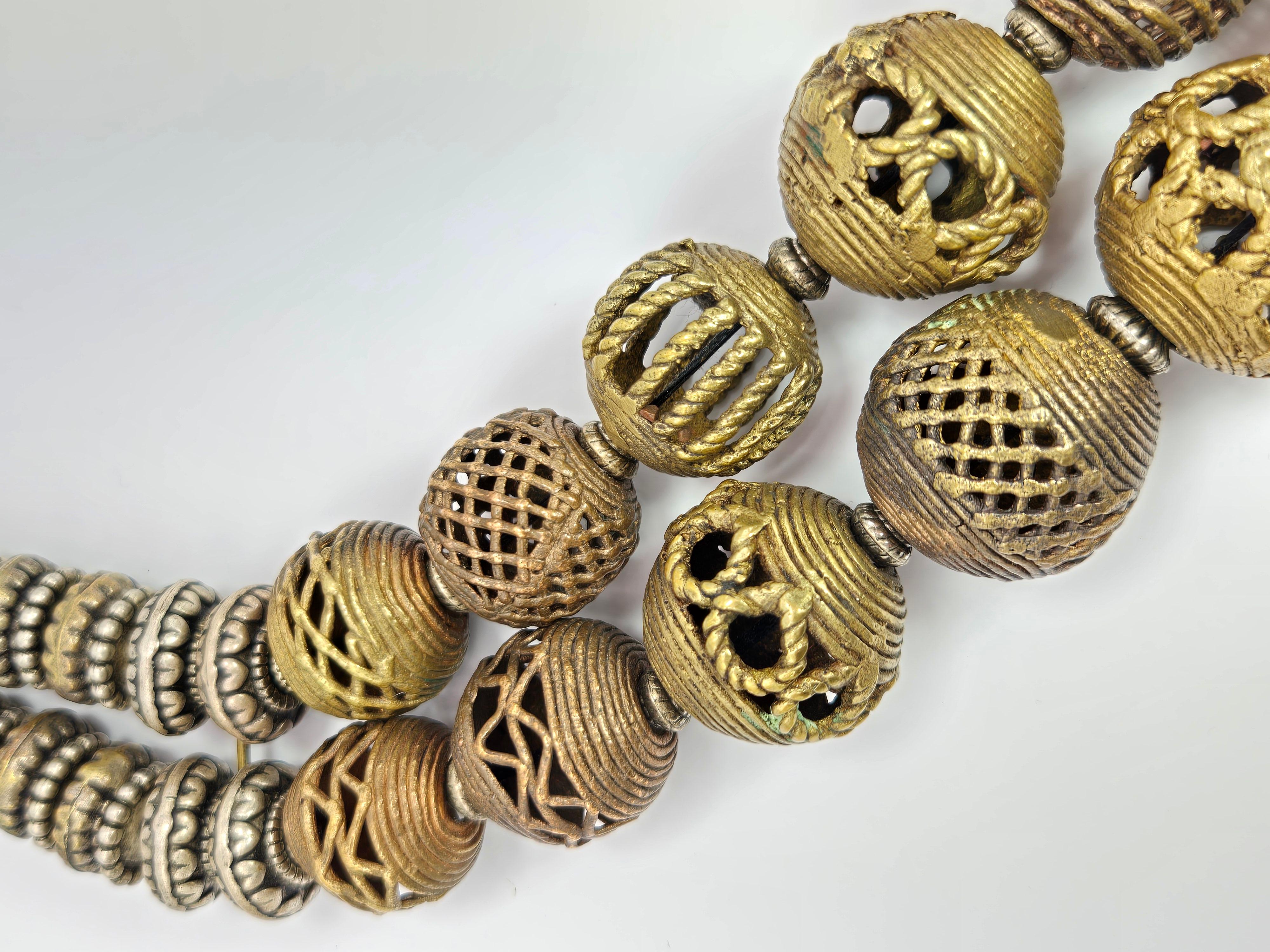 Ce collier à double brin de Masha Archer est composé de perles ajourées en bronze avec des rayures en croix et en spirale provenant des tribus Baoulé du Cameroun. La chaîne de fermeture se termine par une pièce de dix cents des Indes orientales