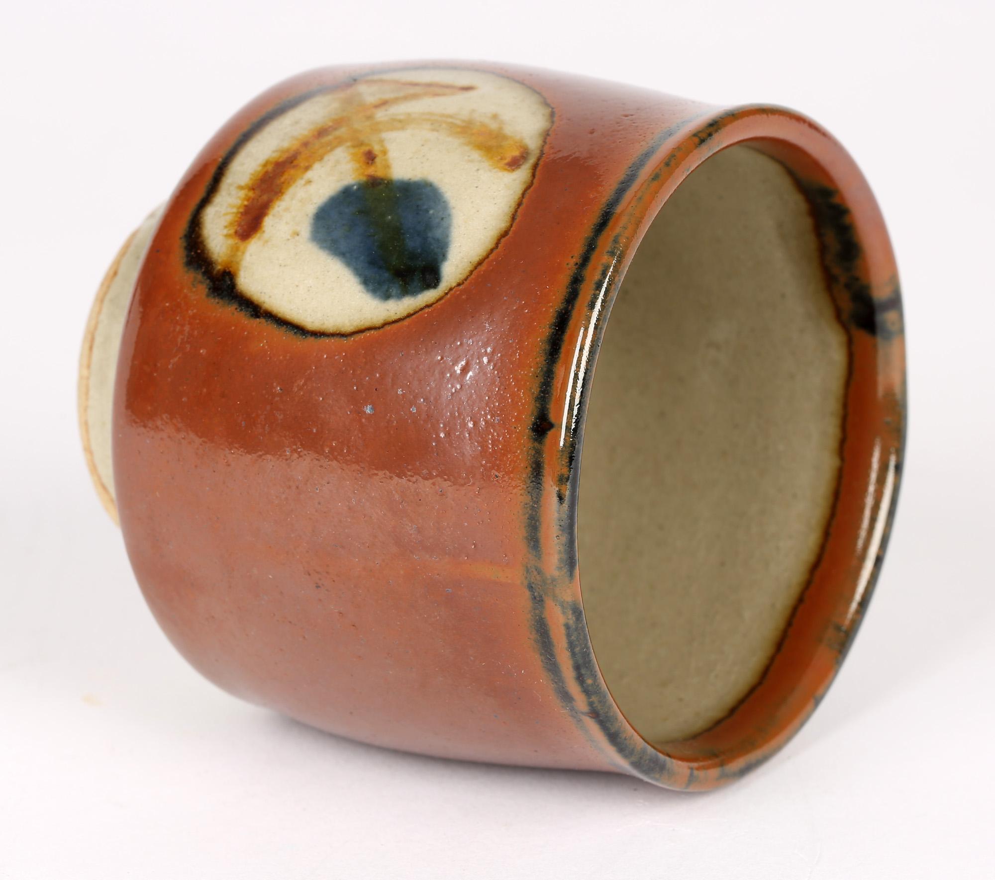 A very stylish Japanese Mashiko Yaki studio pottery Yunomi with stylized designs in panels set within a brown glazed body in the manner of Shoji Hamada and dating from around 1960. The small cylindrical shaped cup stands raised on a narrow rounded