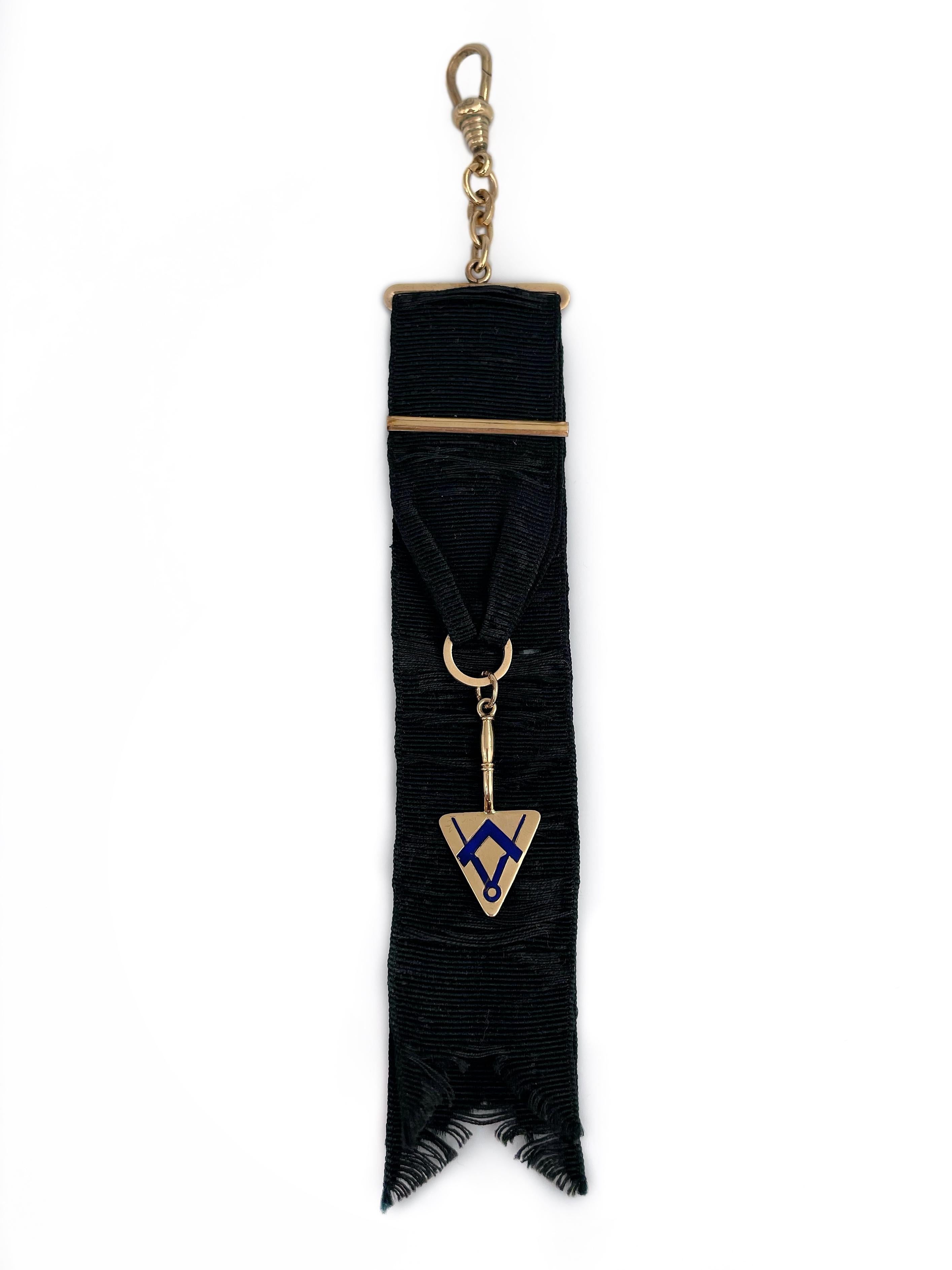 This is a Masonic watch fob pendant. Circa 1930. 

The piece features a black silk grosgrain ribbon. The trowel attached to the fabric is crafted in 18K gold. There is a “square and compasses” symbol inlayed with blue enamel. 

Weight: 6.85g
Ribbon