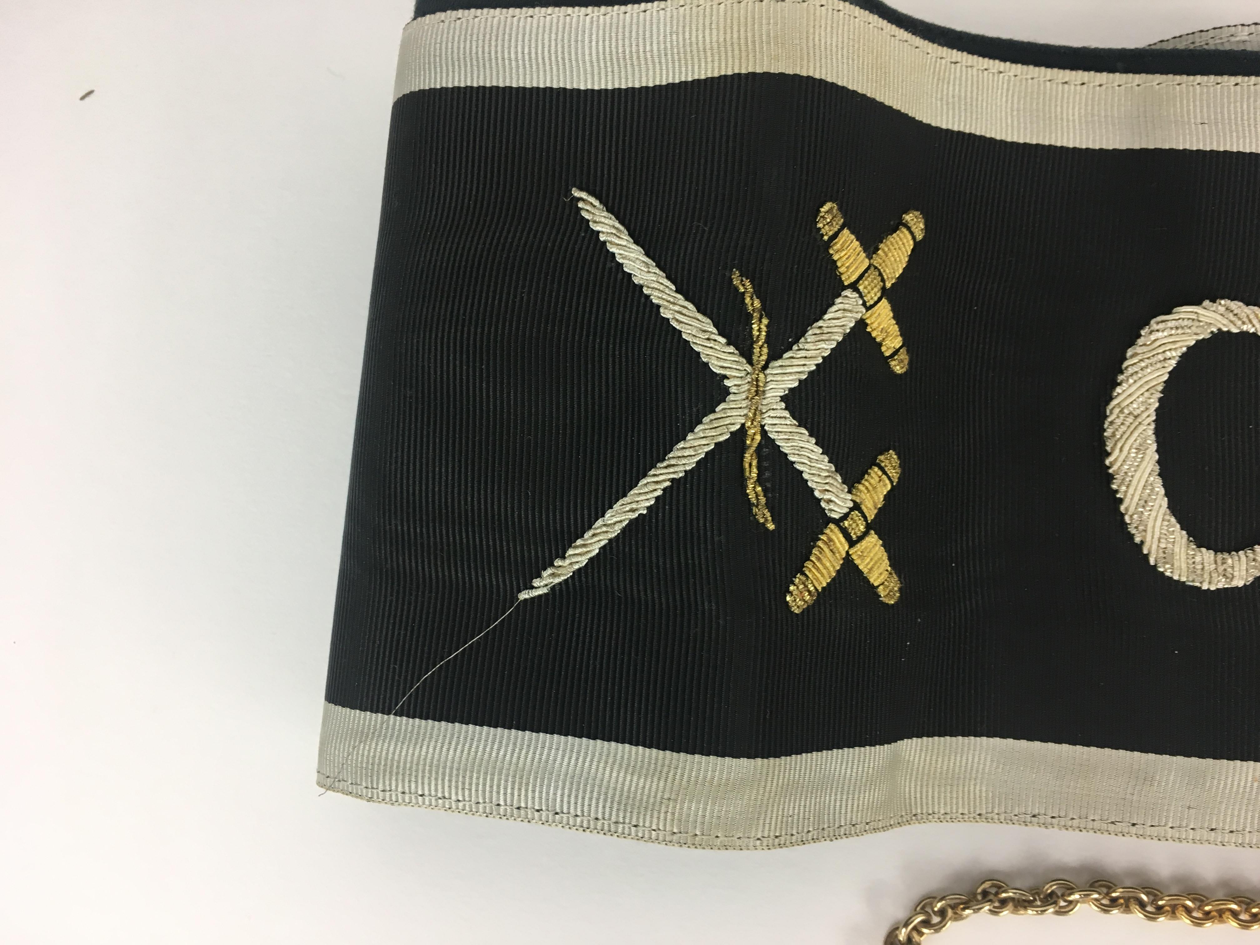 La catena in ottone smaltato del XX secolo e la regalia in panno nero monogrammata erano indossate dai Cavalieri Templari della confraternita massonica per le riunioni cerimoniali. In dotazione un calamaio in peltro e vetro, un accendino e altri due