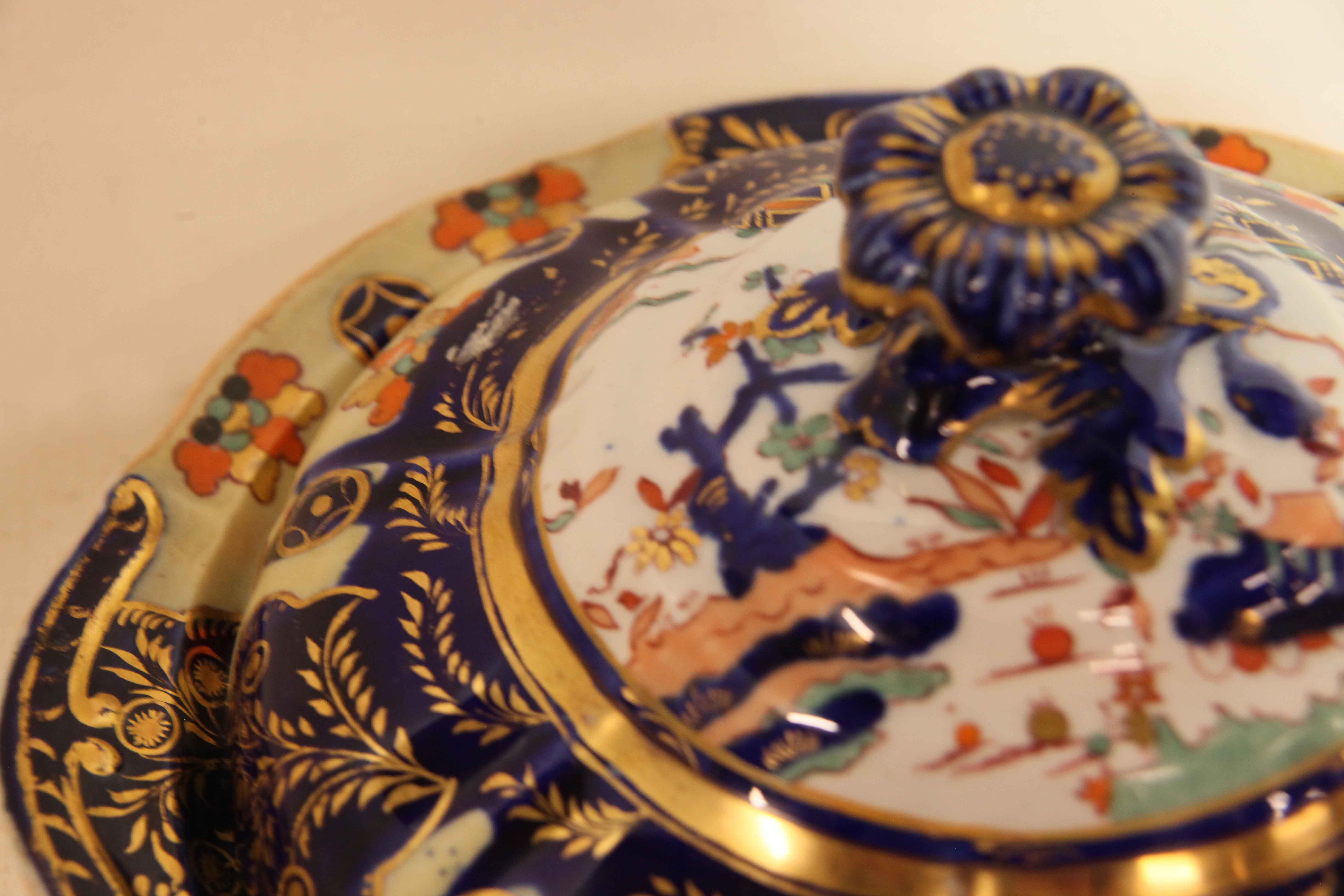 Mason's Ironstone tureen, the upper portion of the lid with finial and oriental motifs on a white background, lower portion with stylized flowers and foliage in various colors and gilding on a creamy yellow and cobalt background; Mason's mark on the