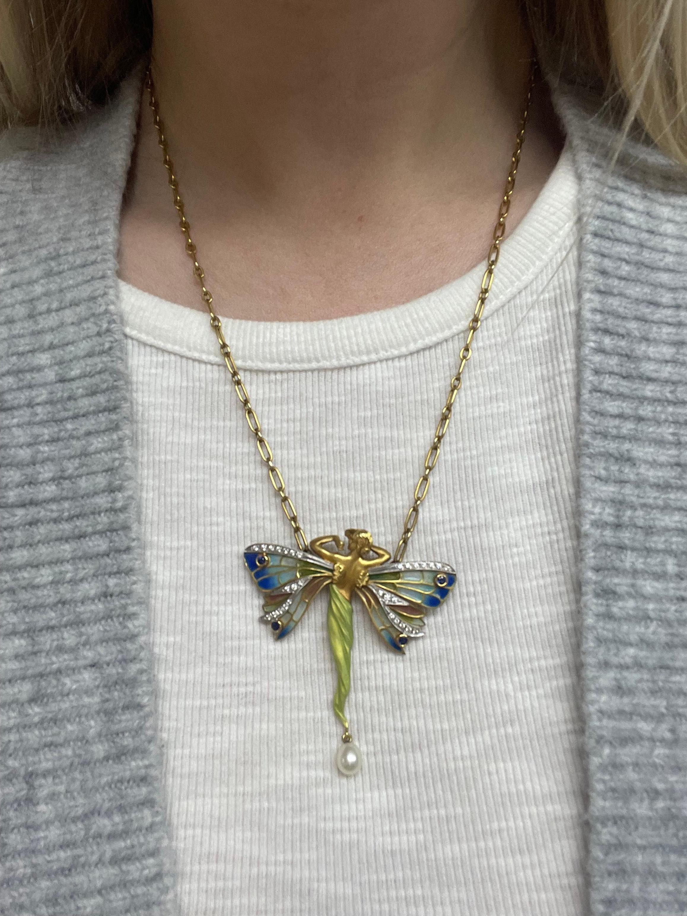 This beautiful pendant brooch necklace designed by Spanish designer Masriera in an Art Nouvea style, depicts a nymph with colorful plique a jour wings decorated in diamonds and sapphires, a green opalescent enamel garment with a cultured pearl drop.
