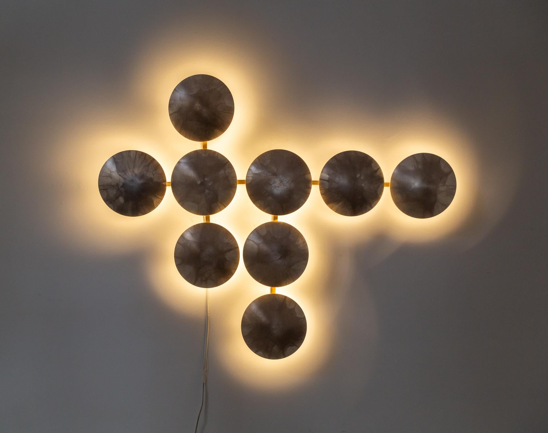 A large backlit sconce comprised of nine burnished, silver-tinted brass convex disks designed by Massimo Castagna and created by Henge. 
It looks like a sculptural wall installation and can be oriented horizontally or vertically.  Made with LED