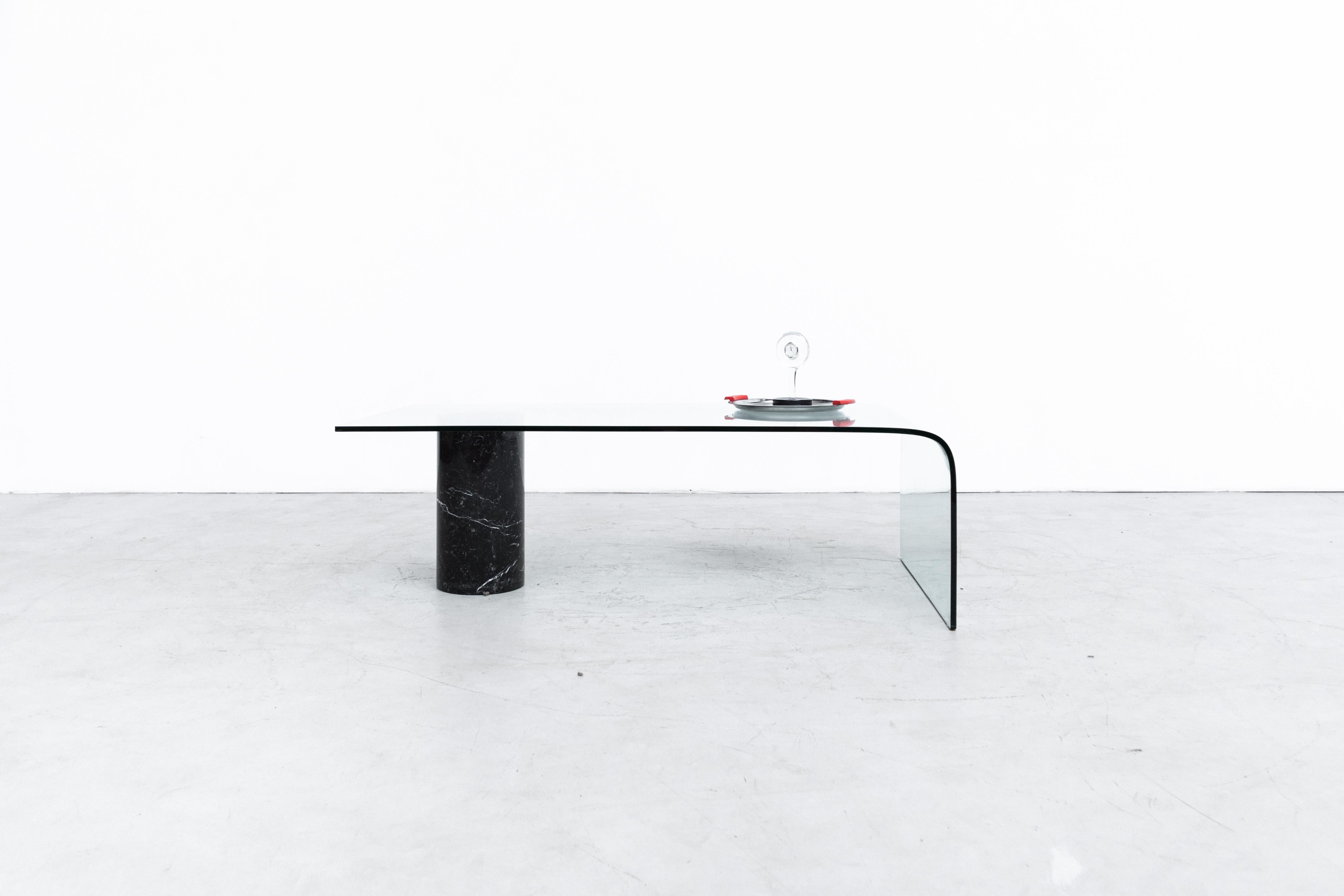 Modern Massimo Vignelli Inspired coffee table with bent glass and heavy black marble support. In good overall original condition with some wear and scratching. More are available with chipping to the glass.