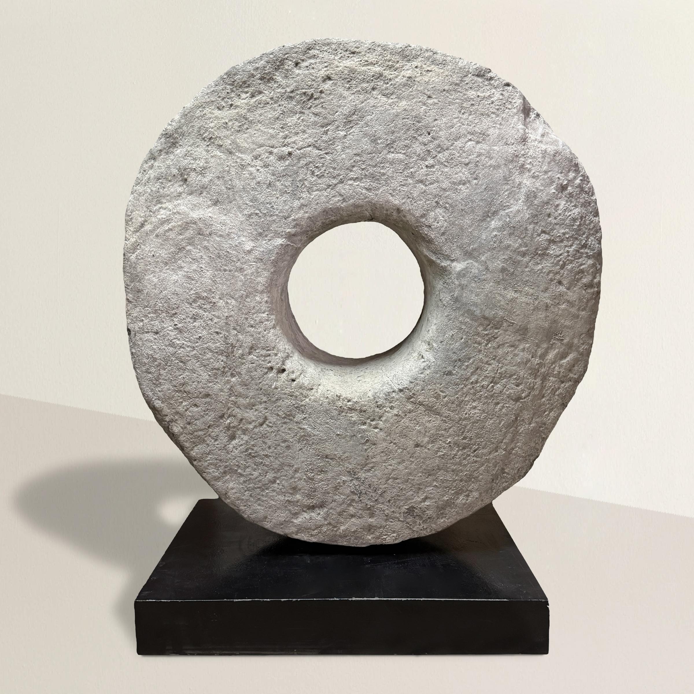 Monumental in scale and presence, this 18th-century French carved limestone grinding stone has been reimagined as a sculptural object of striking simplicity. Mounted vertically on a custom steel stand, the massive 10-inch-thick limestone ring