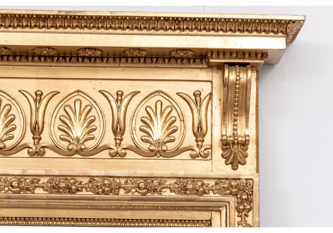 A large and impressive mirror with a carved cornice with leafy bands and rosettes underneath. The wide top frieze with a band of palmettes framed by scrolled brackets. The surround on the top and sides with pendant fruit clusters and an inner