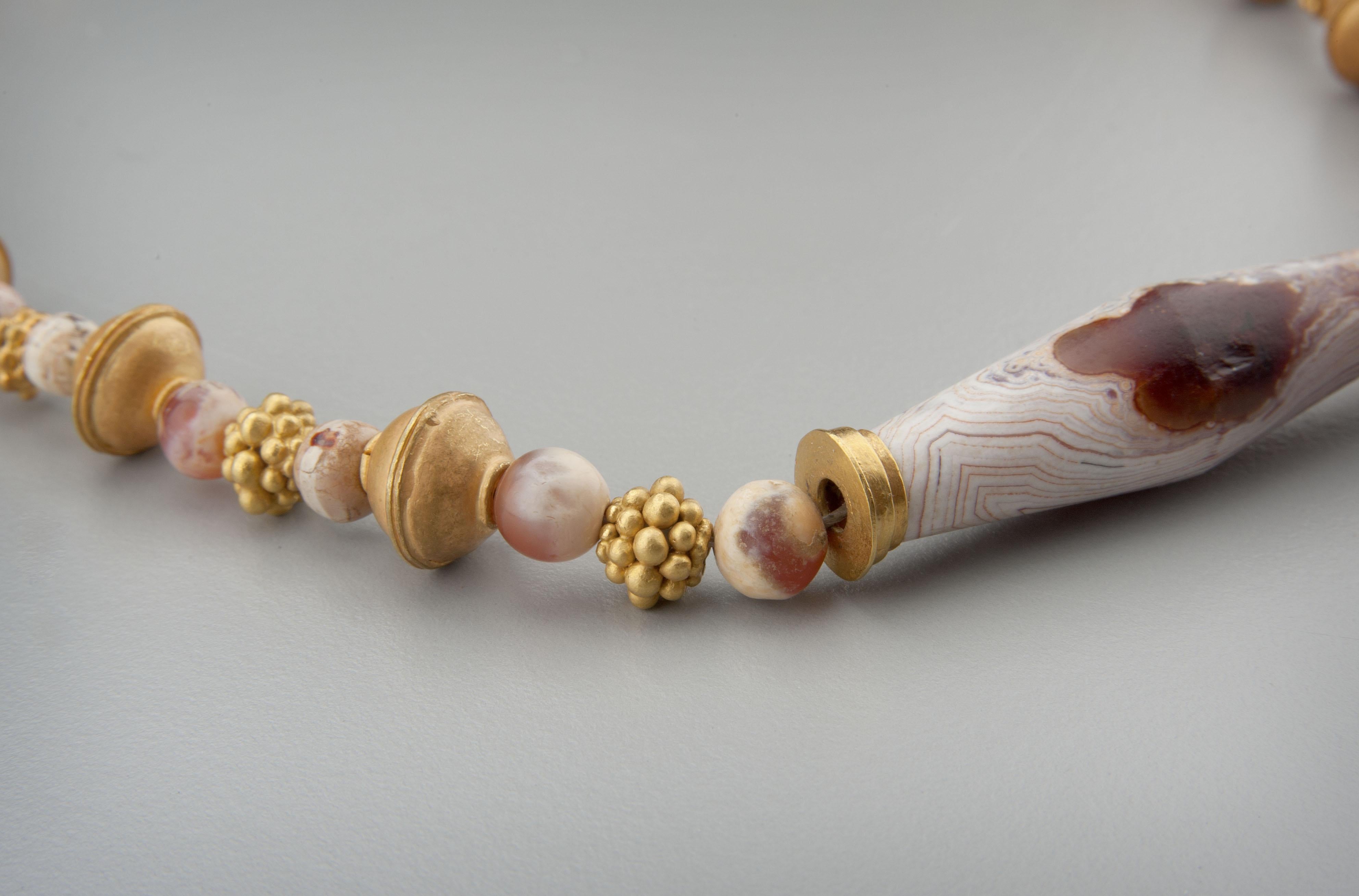 A necklace of gold beads of two designs alternating with round and short barrel agate and carnelian beads with a large gold capped agate bicone tube bead at the center of the necklace. All the stone beads have been whitened from burial in alkaline