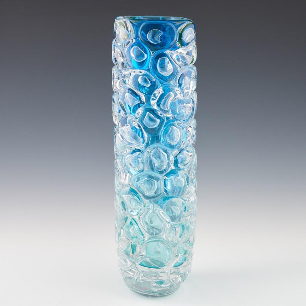 Heading : Allister Malcolm Luminescent Aqua Bubble Wrap Cylindrical Vase
Date : 2023
Origin : Stourbridge
Bowl Features : Aquamarine internal transitioning to clear with a fine coating of uranium. Applied disc shaped prunts with trapped air