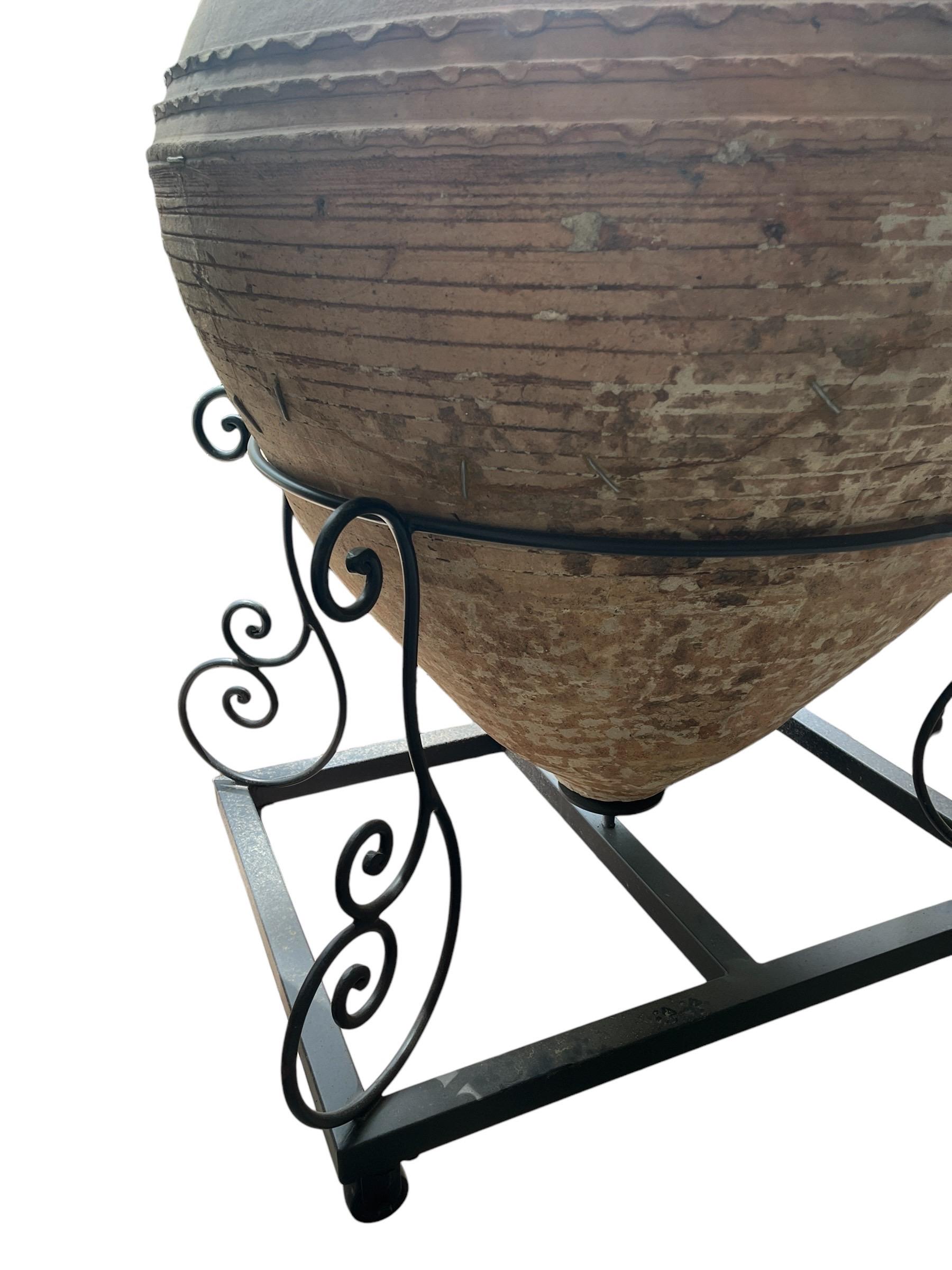 Dieses außergewöhnliche Stück verbindet nahtlos die Antike mit der Moderne. Diese mediterrane Weinamphora-Vase ist aus strapazierfähiger Terrakotta gefertigt und strahlt zeitlosen Charme aus. Er ruht auf einem schlanken Rollensockel aus Metall und