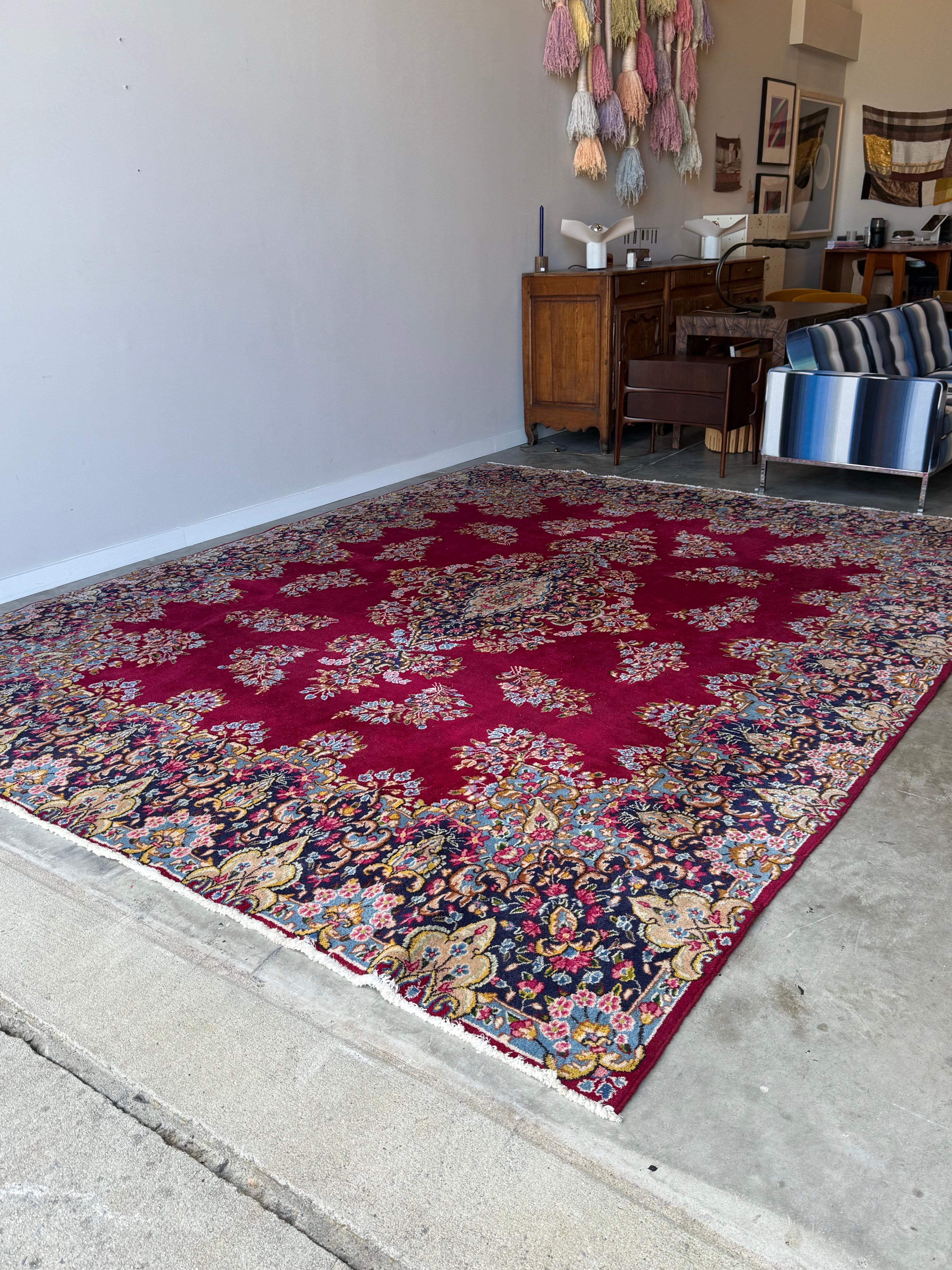 This stunning and very large Persian antique hand knotted rug is a masterpiece of traditional craftsmanship, featuring a rich, deep red field that serves as a captivating backdrop for its intricate design. At the heart of the rug lies an elaborate
