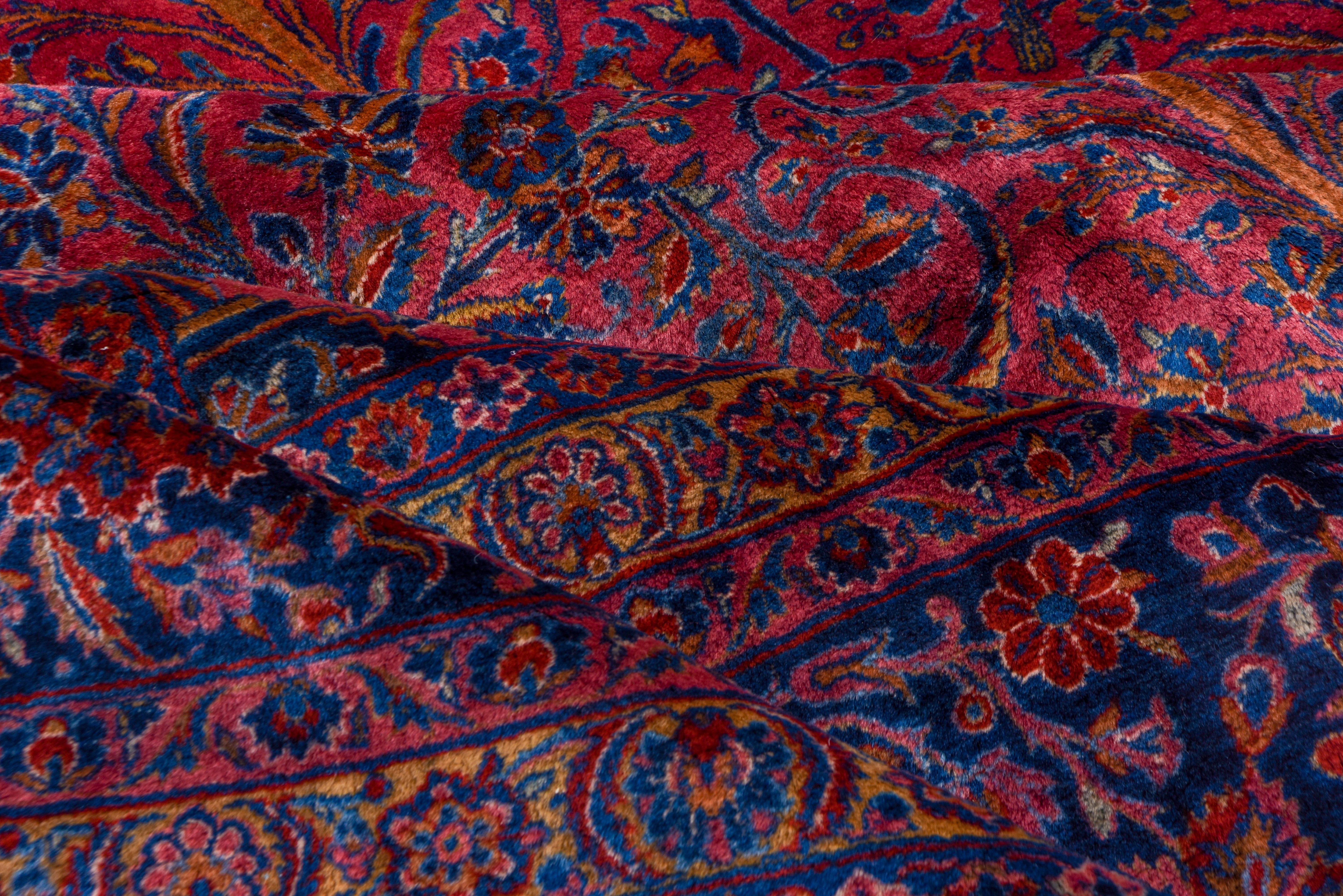 This ruby red ground, royal blue border Manchester wool central Persian city carpet, is absolutely characteristic of the type and period, with a fine weave and velvety surface texture. The all-over pattern of vases, leaves, stems and flower sprays