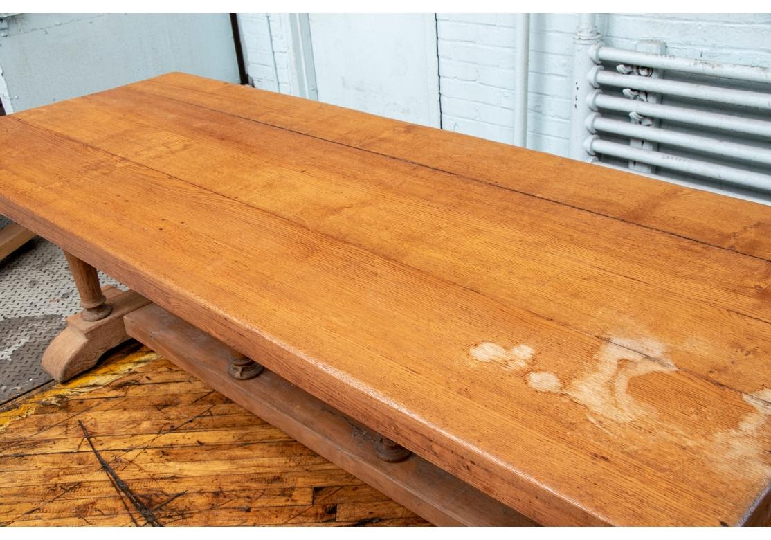 Une grande table de ferme primitive avec une grande forme et un poids pour la restauration. Avec un dessus construit en longues planches. Chaque extrémité est soutenue par deux lourds pieds tournés sur des bases inclinées vers l'extérieur. Le long