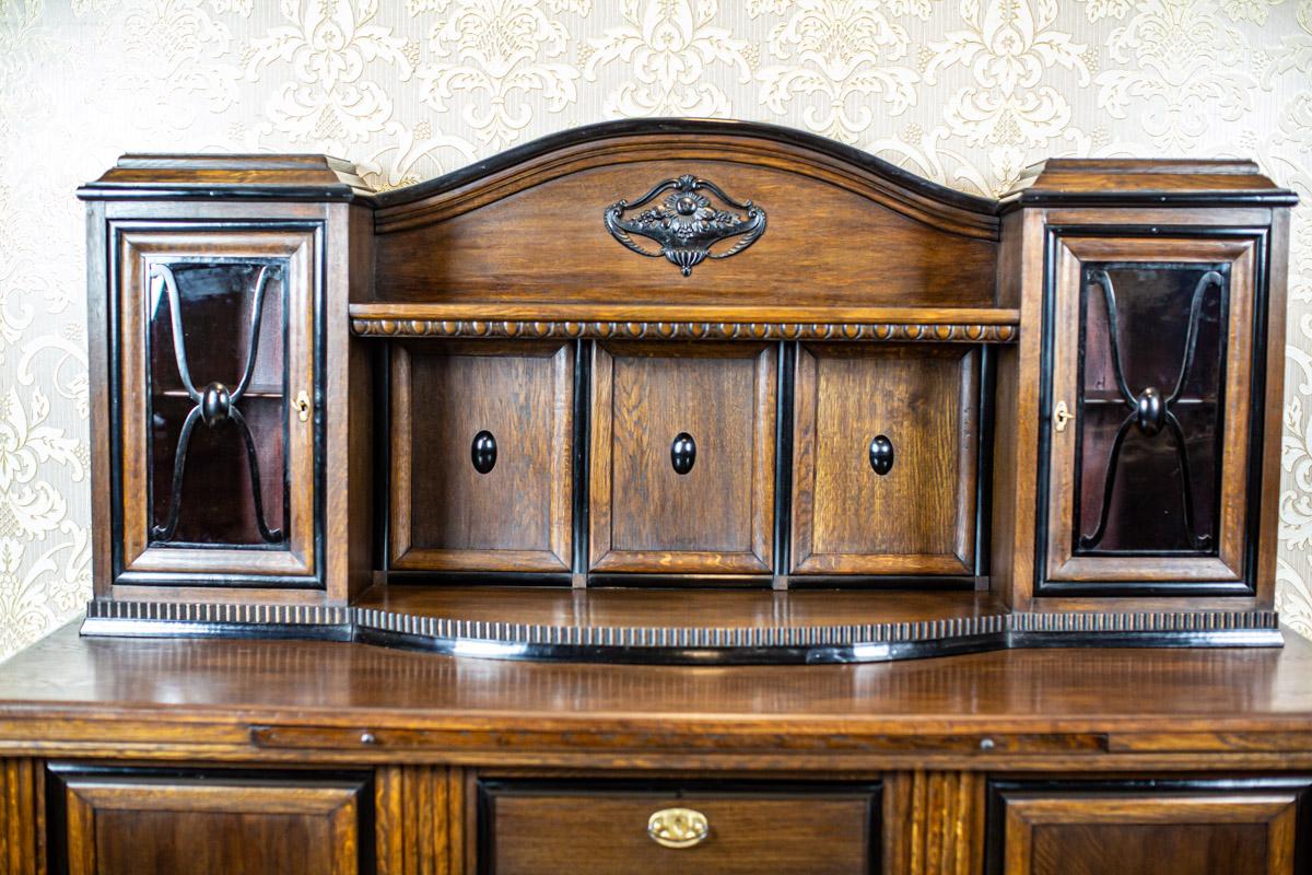 Grand Oak Veener Buffet From the Interwar Period

A large, elegant buffet in a brown color. The piece consists of a double-door base with four drawers. Beneath the main countertop, there is a pull-out auxiliary shelf. The upper section features a