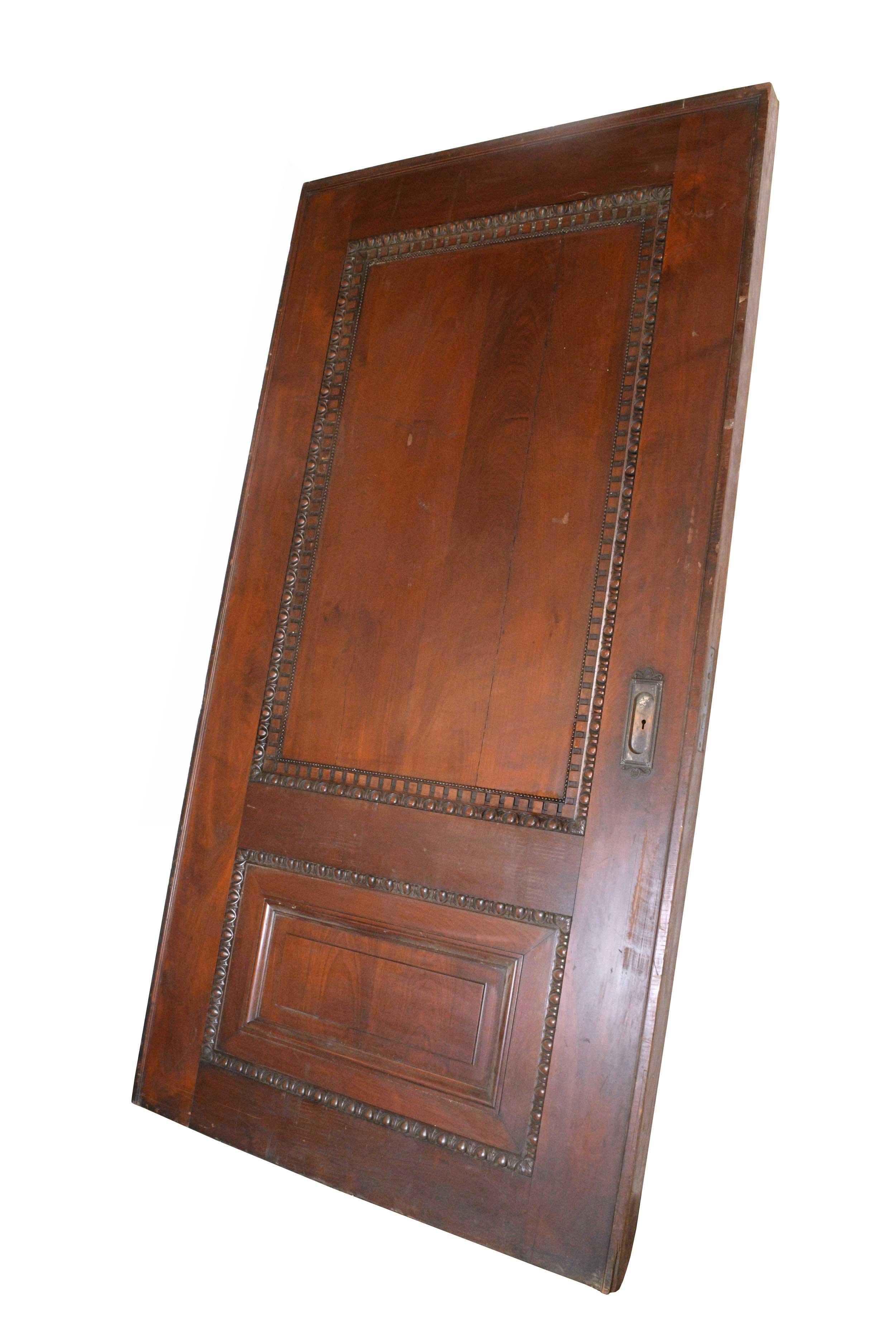 Impressive and stately carved oak pocket door over three inches thick. Features egg and dart details, dentil molding, and beading surrounding the recessed panels. Ornate bronze hardware adorns either side. The door is in good condition with a long