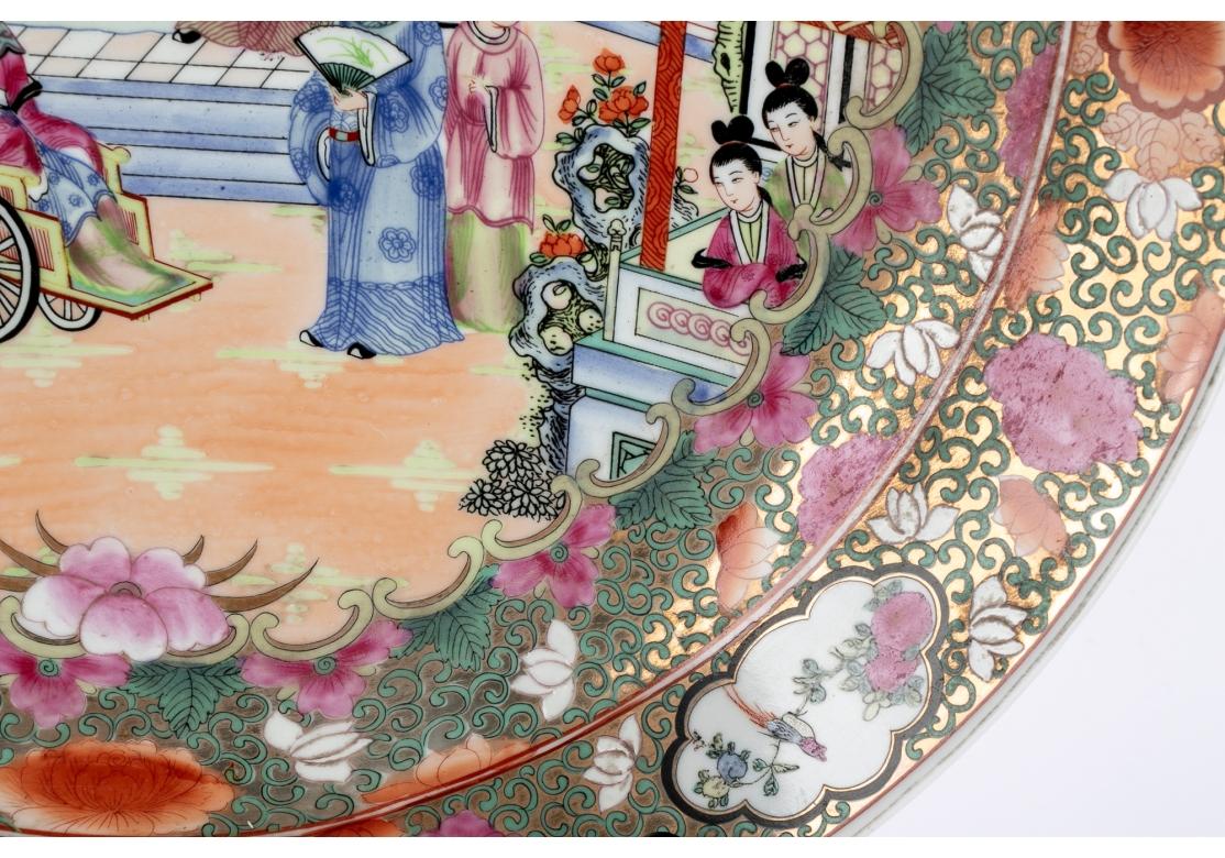 A massive Chinese porcelain charger plate with a central palatial scene with a gentleman under the structure and the attendants with fans, a woman in a wheel chair to the right and the attendants and other figures in acknowledgment.
The charger