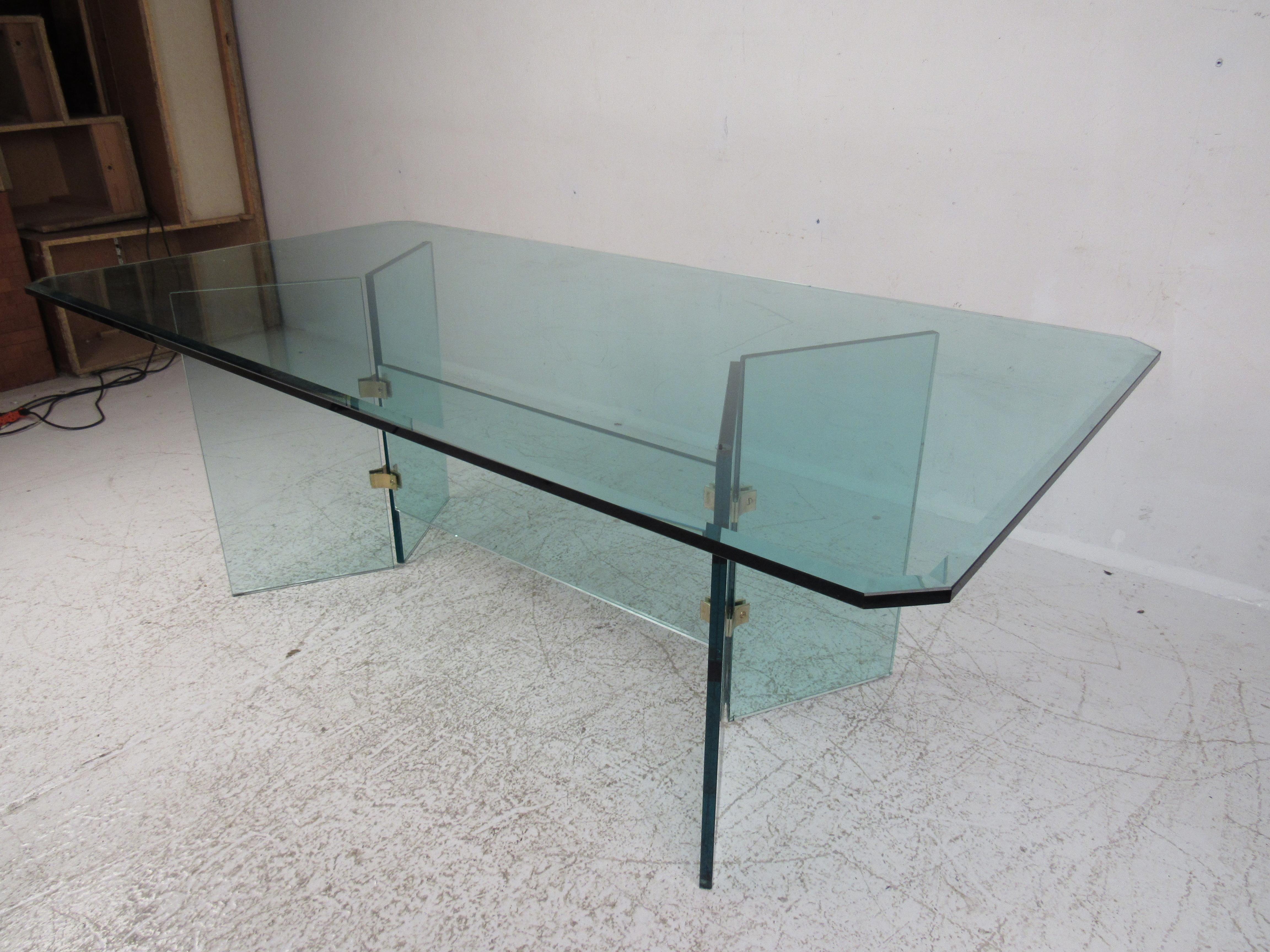 An ingenious modern design made with extremely thick beveled glass and brass fixtures. This midcentury style dining table boasts a 78 inch wide glass top offering plenty of room for guests. A sturdy base with five thick pieces of glass held together