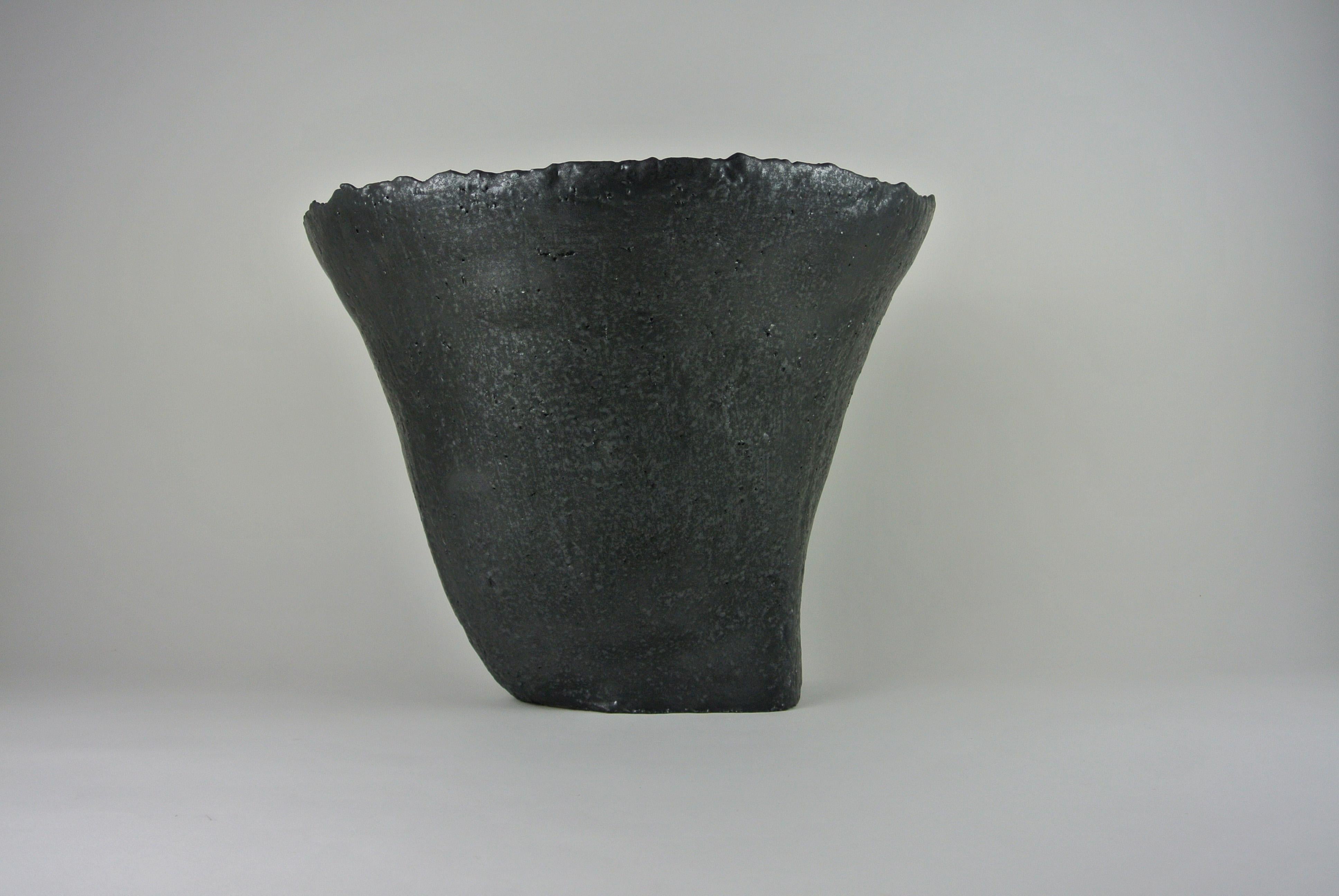 Massive asymmetric vessel in grey, rough stoneware with black metallic glaze. Fire sand texture visible on surface. Available with or without flower tray.
All pieces by Christine Roland celebrate the imperfections that occur from working with a