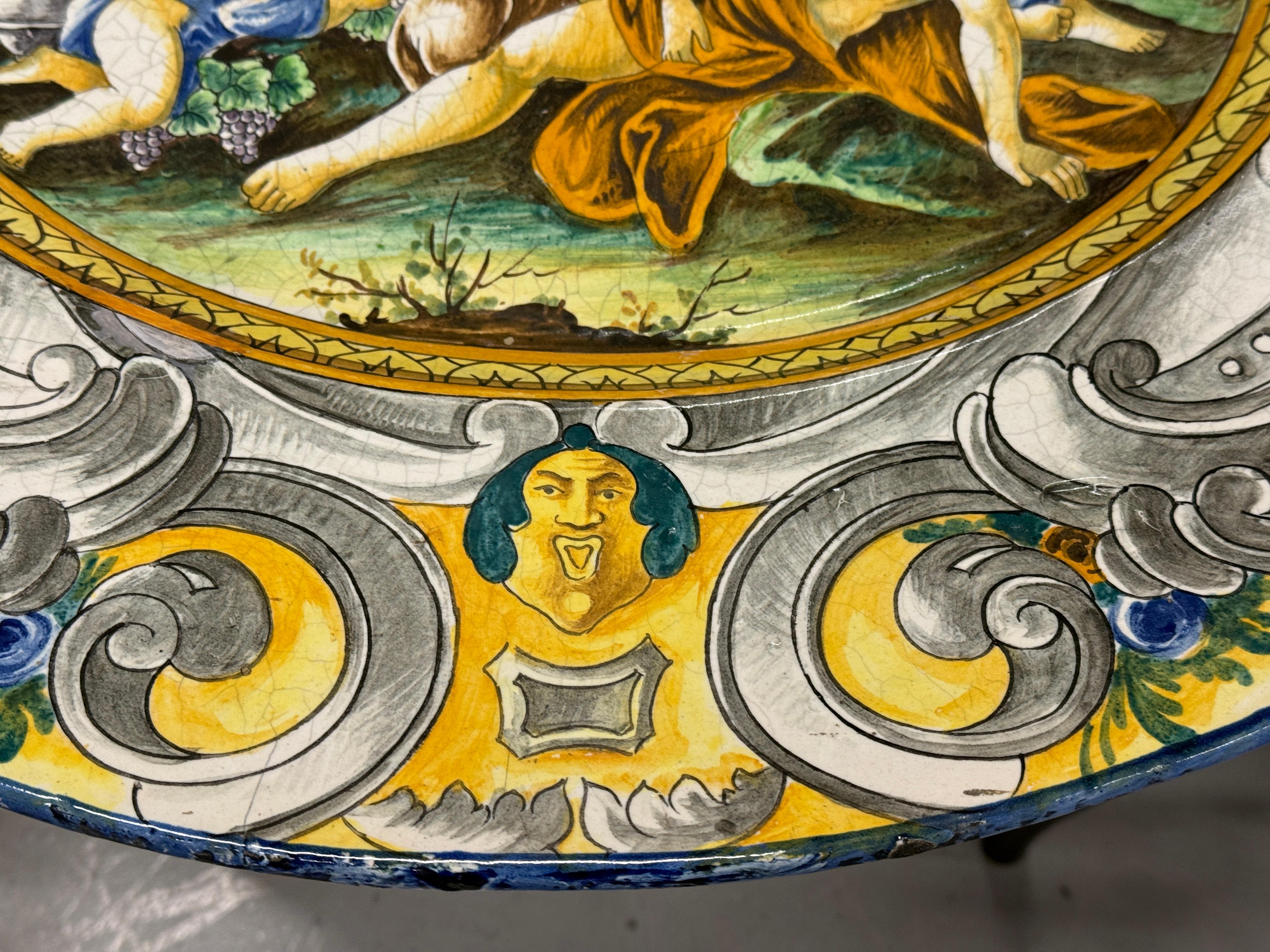 Plat massif en faïence émaillée à l'étain de la région de Deruta en Italie. Le plat représente une scène de bacchanales et date du début du 20e siècle. Le plat est signé d'un monogramme au dos et de la mention Italia. Il est magnifiquement peint et
