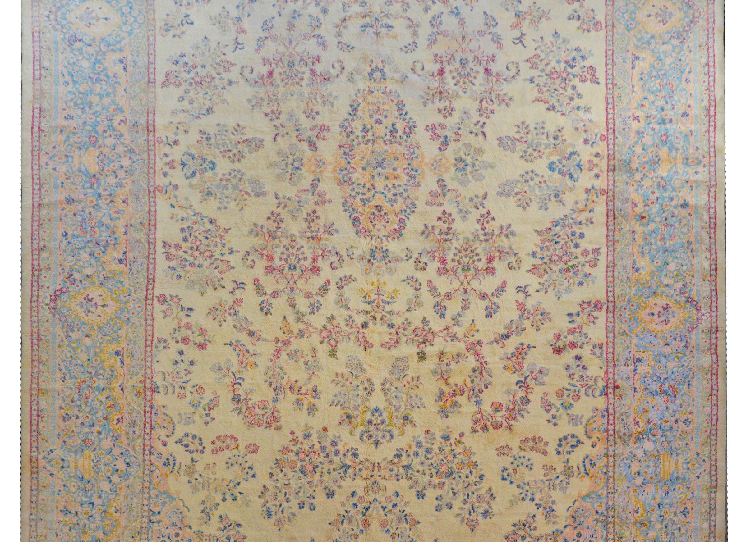 A massive early 20th century Persian Kirman rug with a wonderful all-over floral and leaf pattern woven in pink, light indigo, gold, pale green, all on a pale yellow background. The border is typical with a similarly patterned central stripe flanked