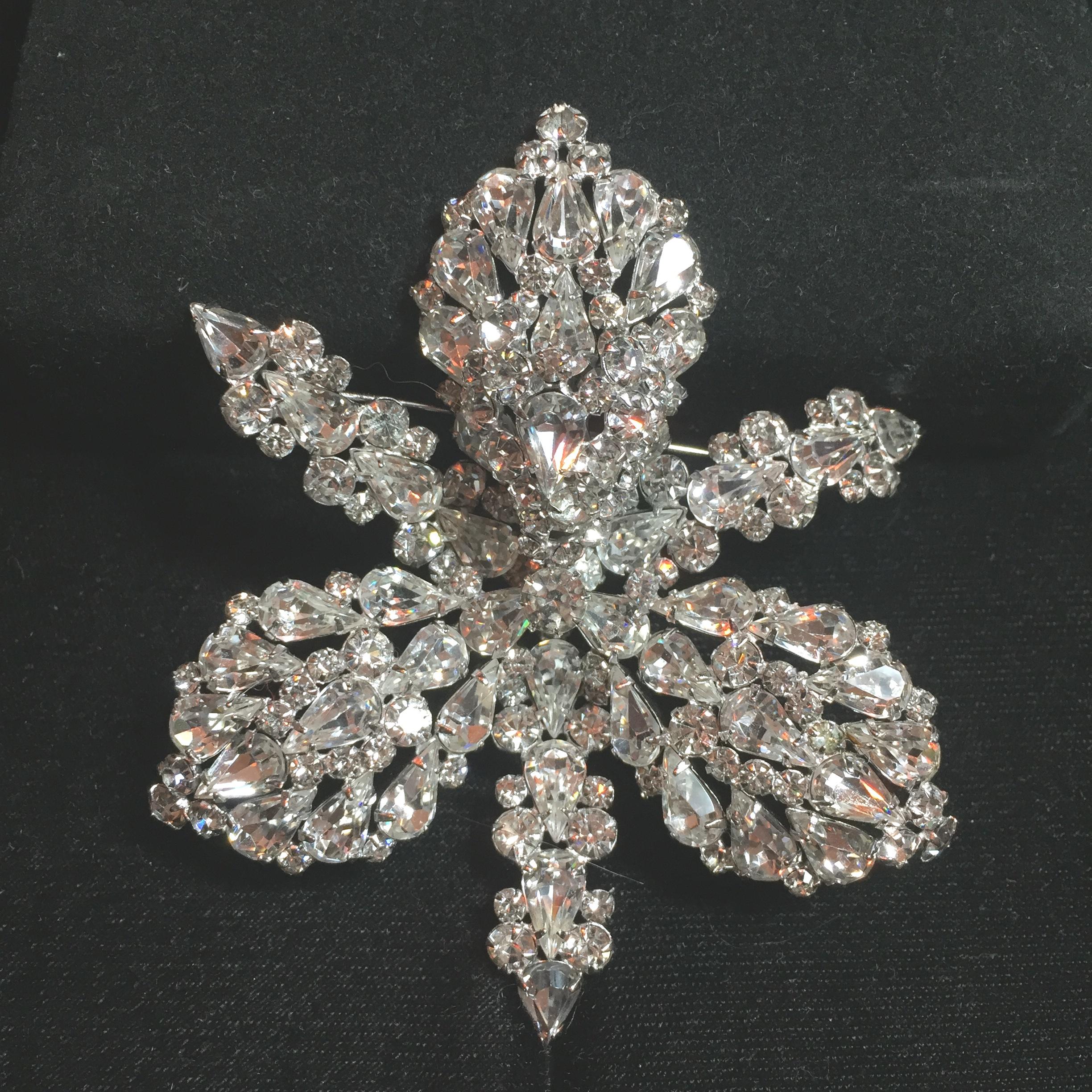 Offered here is a massive Elsa Schiaparelli rhodium-plated brooch and matching clip-back earrings from the 1950s. The exquisitely engineered hand-soldered three-dimensional design is that of a three-lobed orchid blossom hand-set with hundreds of