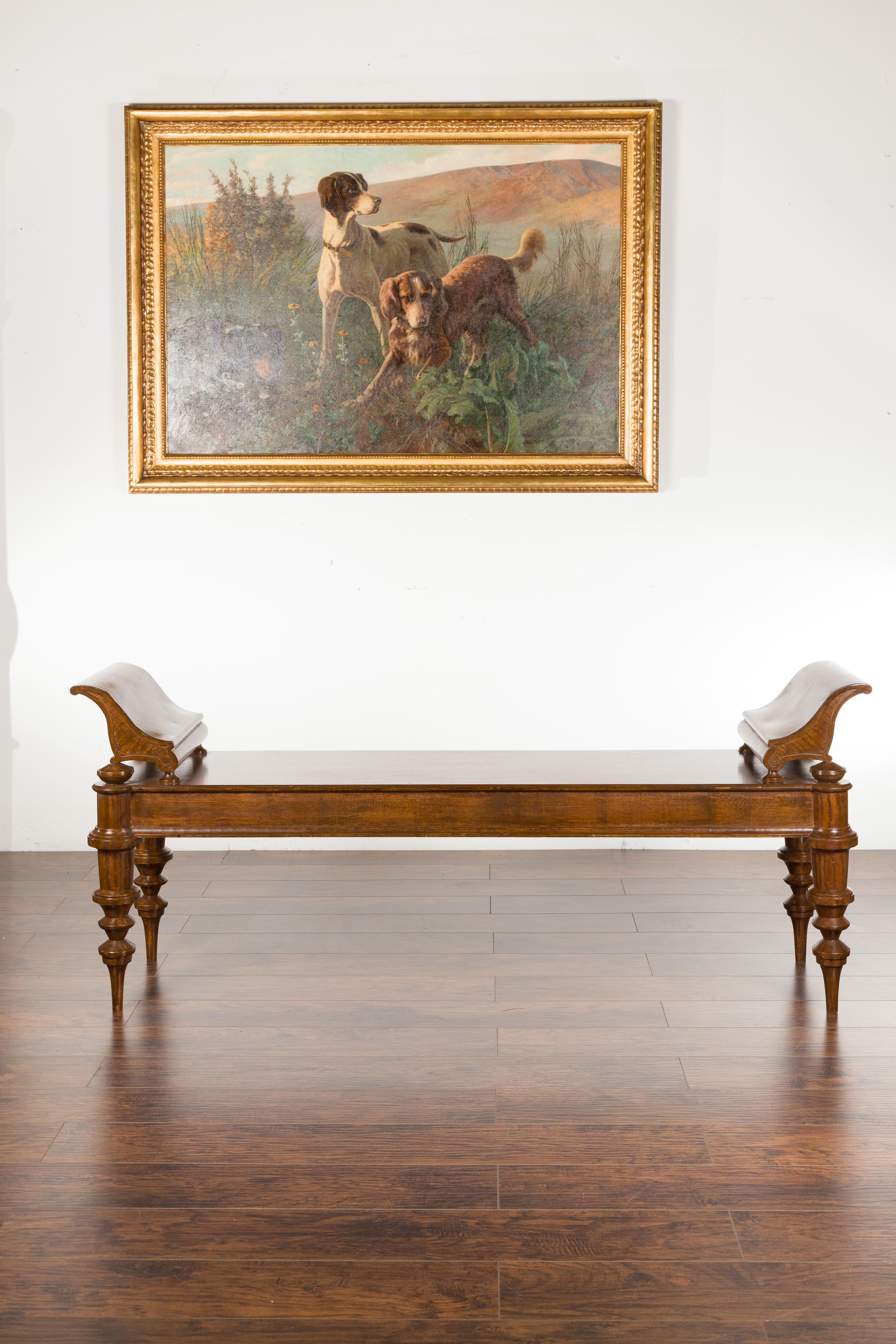 A massive English mahogany bench from the 20th century, with curving arm supports and turned legs. Created in England during the 20th century, this mahogany bench features a long rectangular seat flanked with curving arm supports. Raised on four